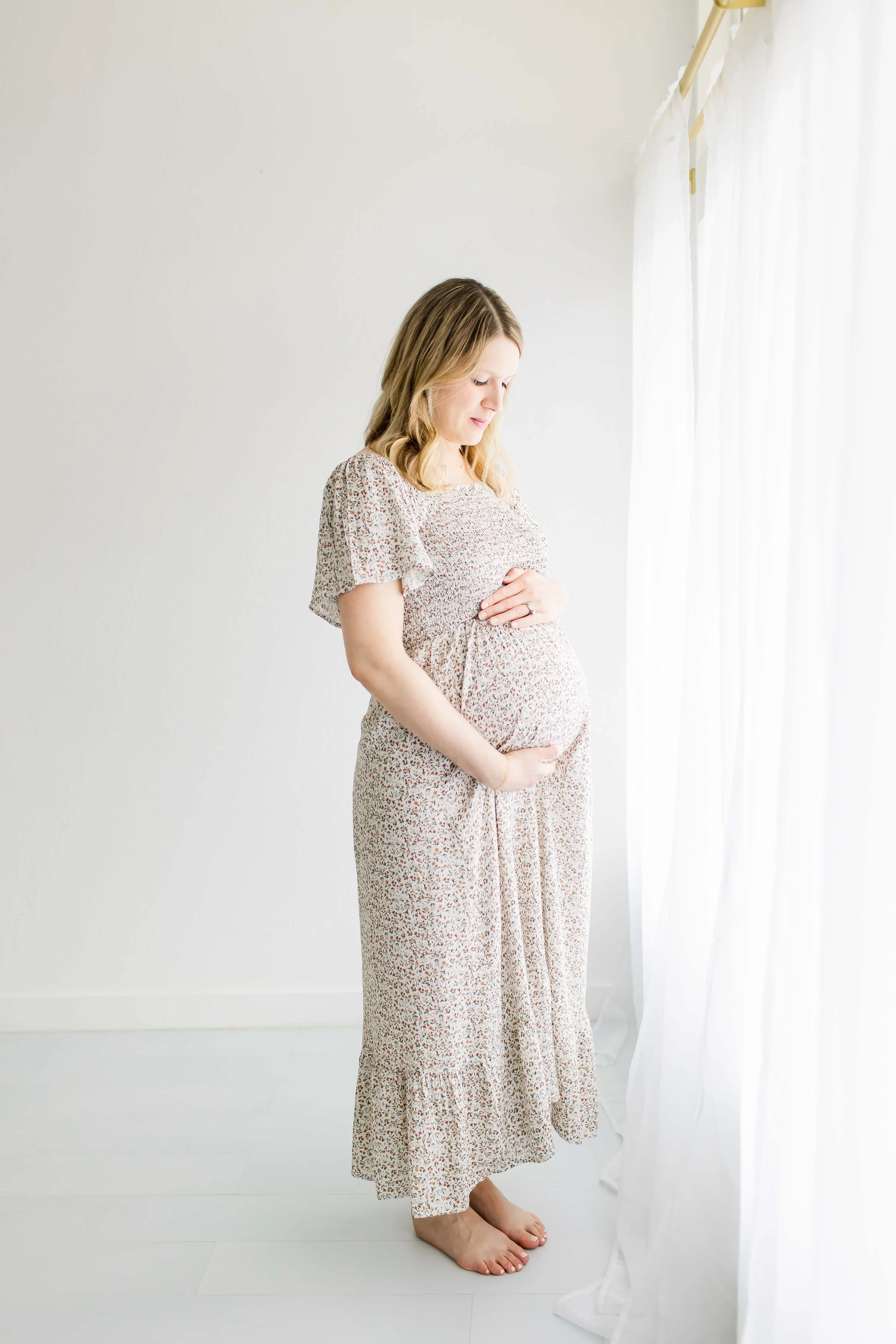 Pregnant mother looking out window at East and Elm Portrait studio in Fairport, NY