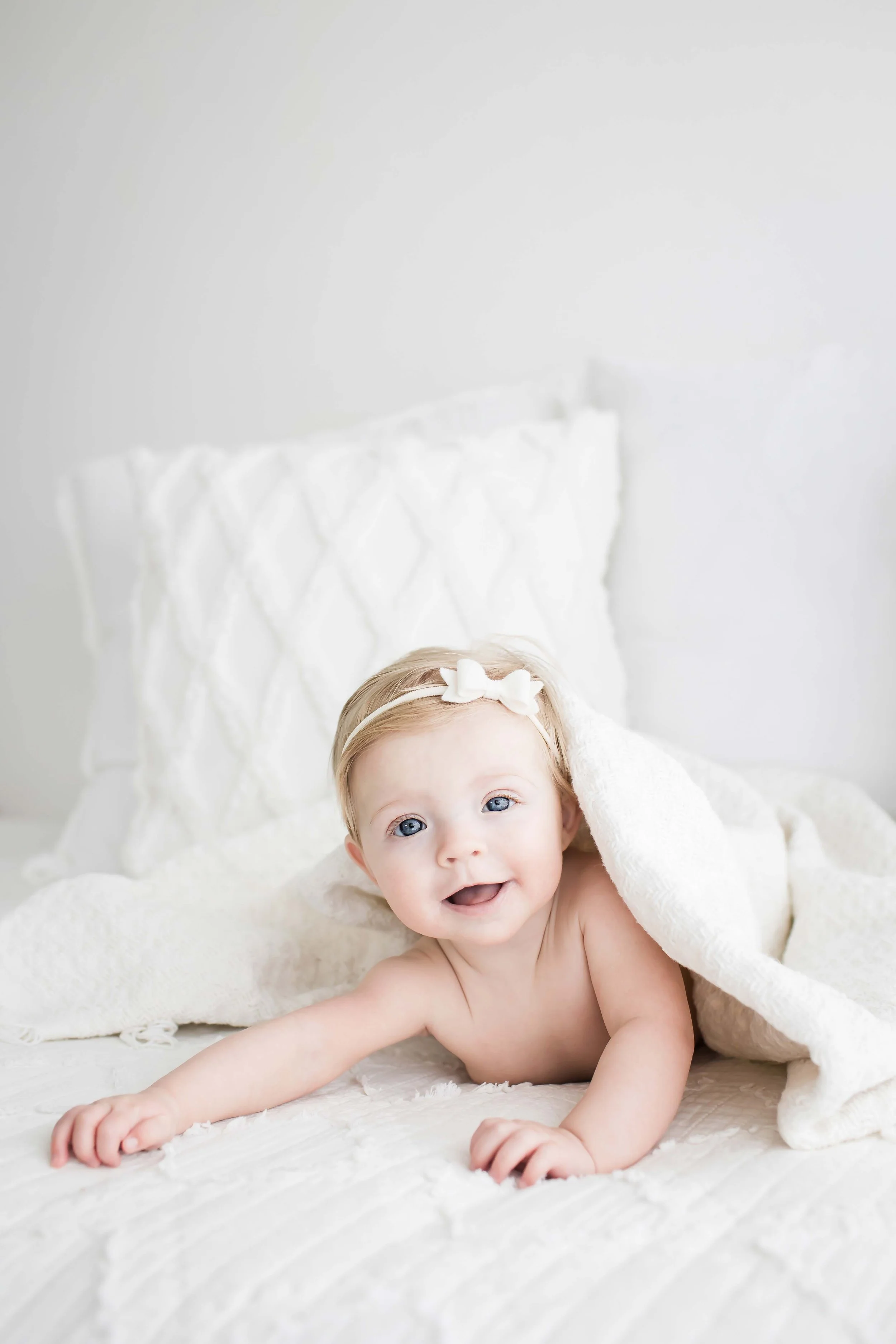 Smiling baby in a white headband reaching forward during a Rochester NY newborn session