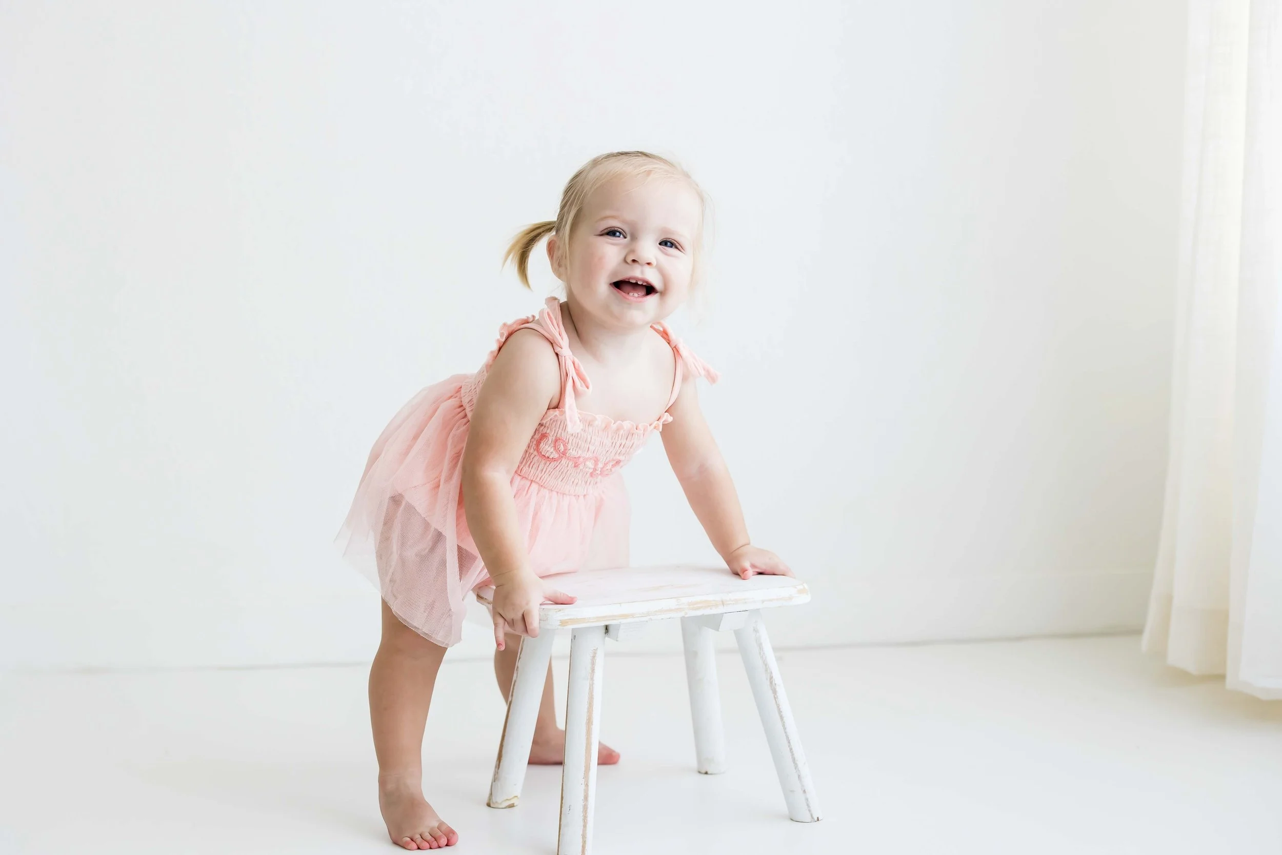 Toddler girl balancing on a small white stool in a bright studio, Fairport NY milestone photography