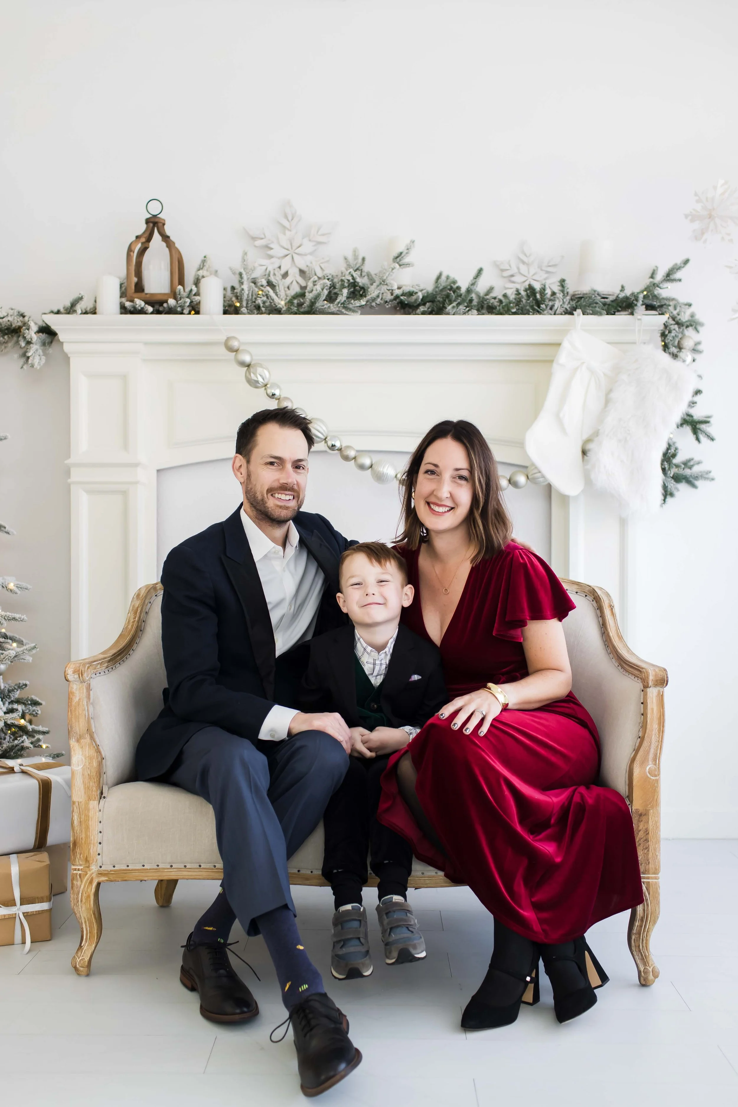 A family of three sitting on a vintage couch during Christmas at East and Elm Portrait Studio in Fairport, NY, during a christmas mini session.