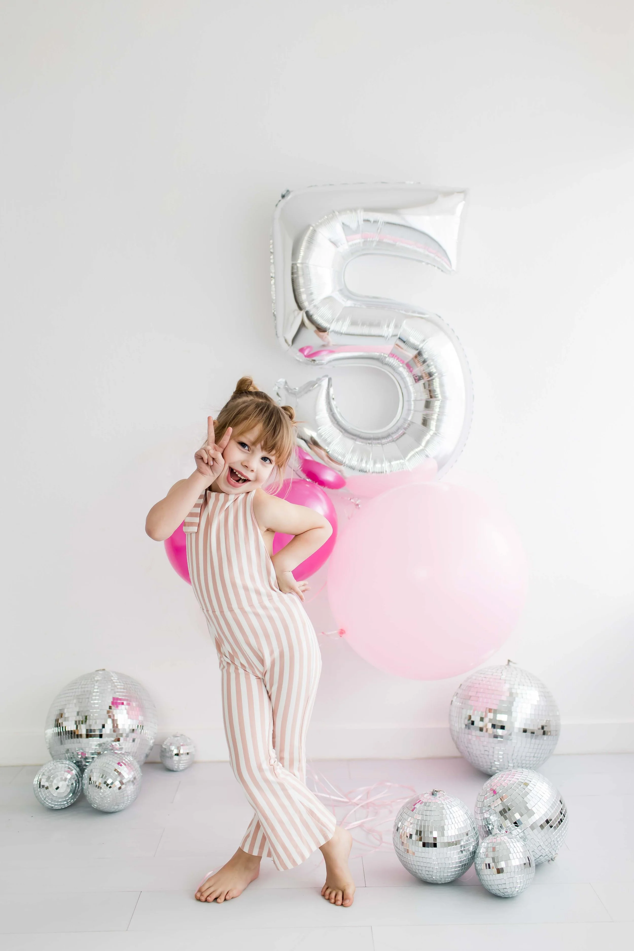 Little girl making a peace sign in striped pajamas surrounded by balloons, Rochester NY birthday photography