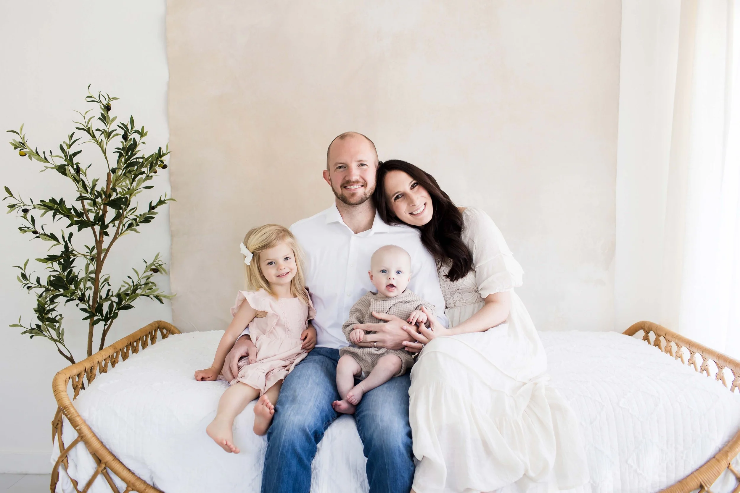 A family of five sitting together on a white bed at East and Elm Portrait Studio during a family session in Fairport, NY.