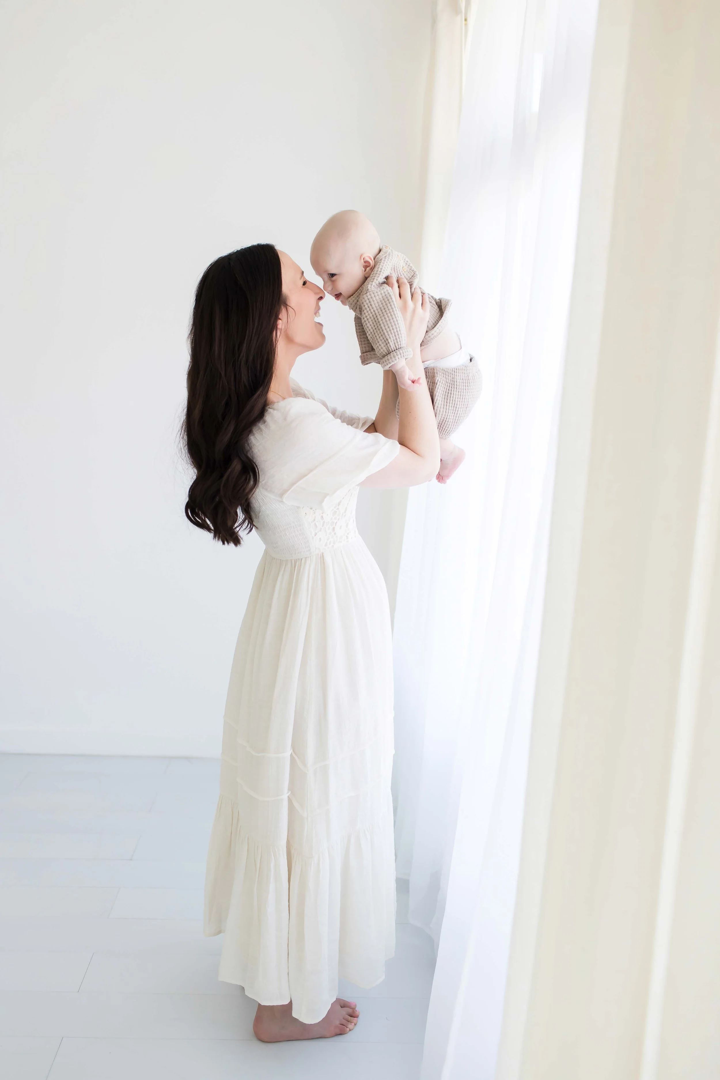 A woman with long dark hair holding a baby face to face, at East and Elm Portrait Studio during an in-studio family photography session in Fairport, NY.