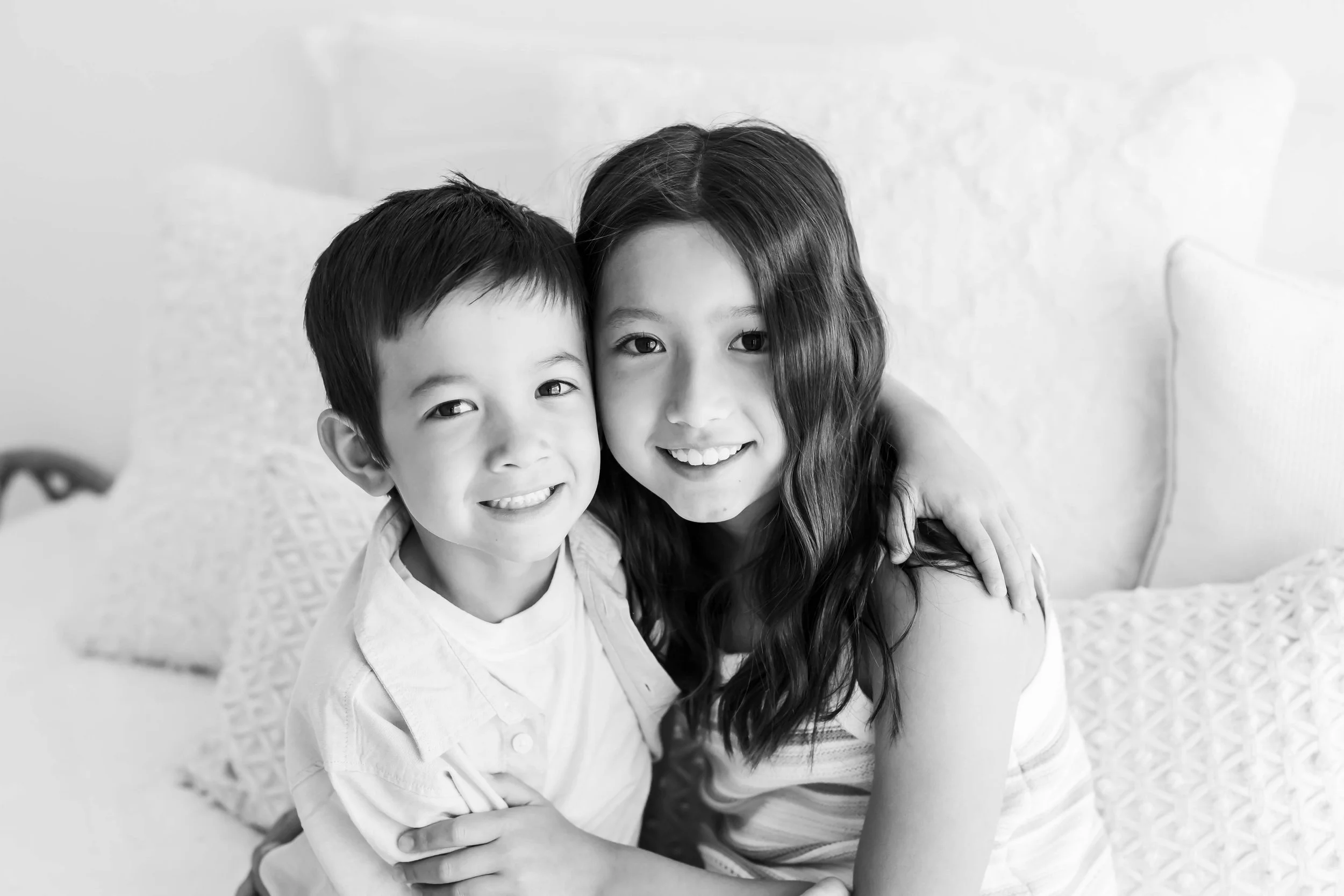 Two kids both sitting on a bed with a textured blanket at East and Elm Portrait studio in Fairport, NY, during family session.