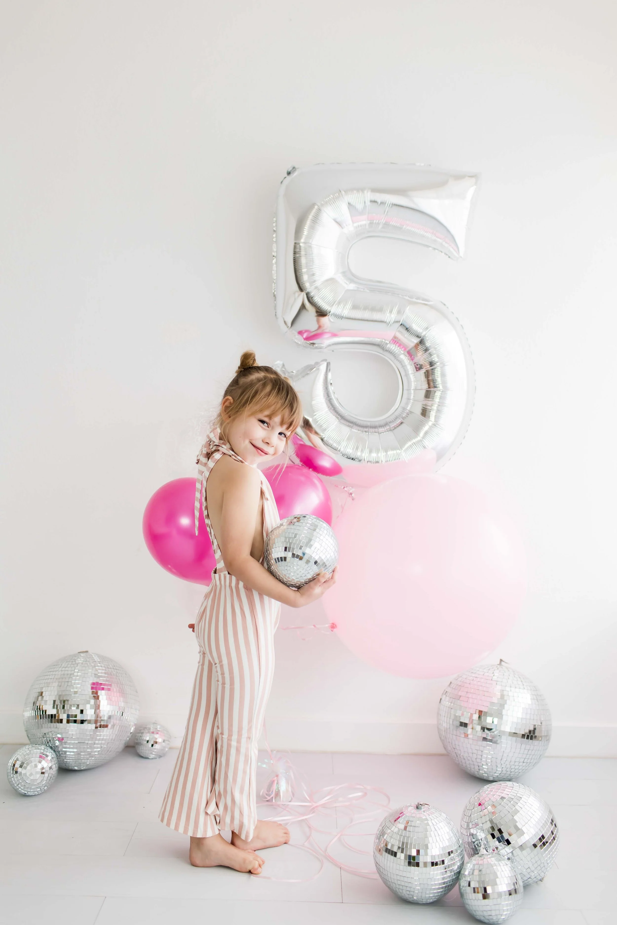 Little girl in a pink striped jumpsuit holding a disco ball at her fifth birthday session, Fairport NY