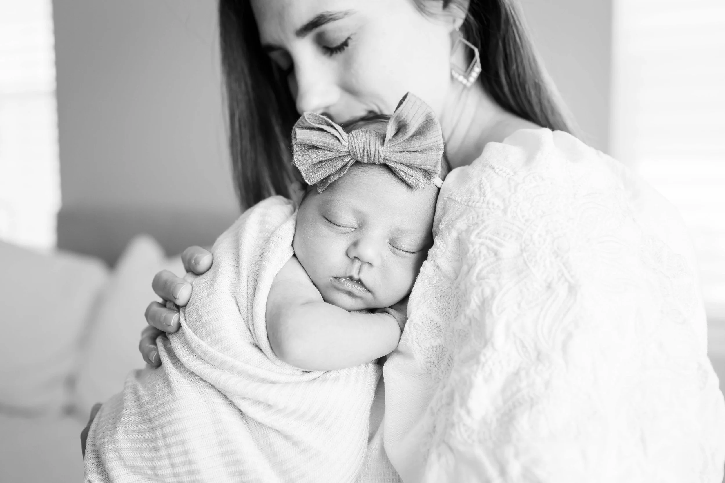 A mom gently holding a sleeping baby with a large bow headband at East and Elm Portrait Studio during a studio newborn photography session in Fairport, NY.