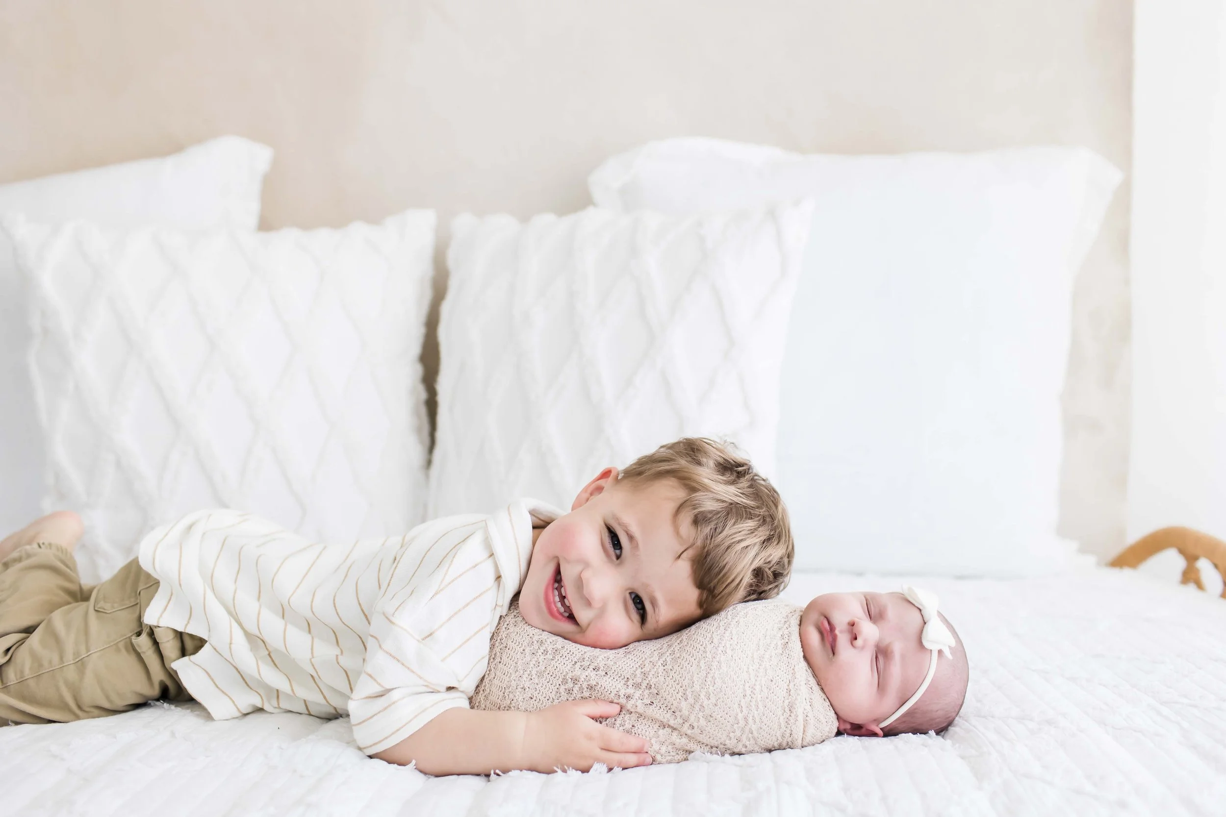 A young boy lying on a bed next to a newborn baby at East and Elm Portrait Studio in Fairport, NY, during a newborn session.