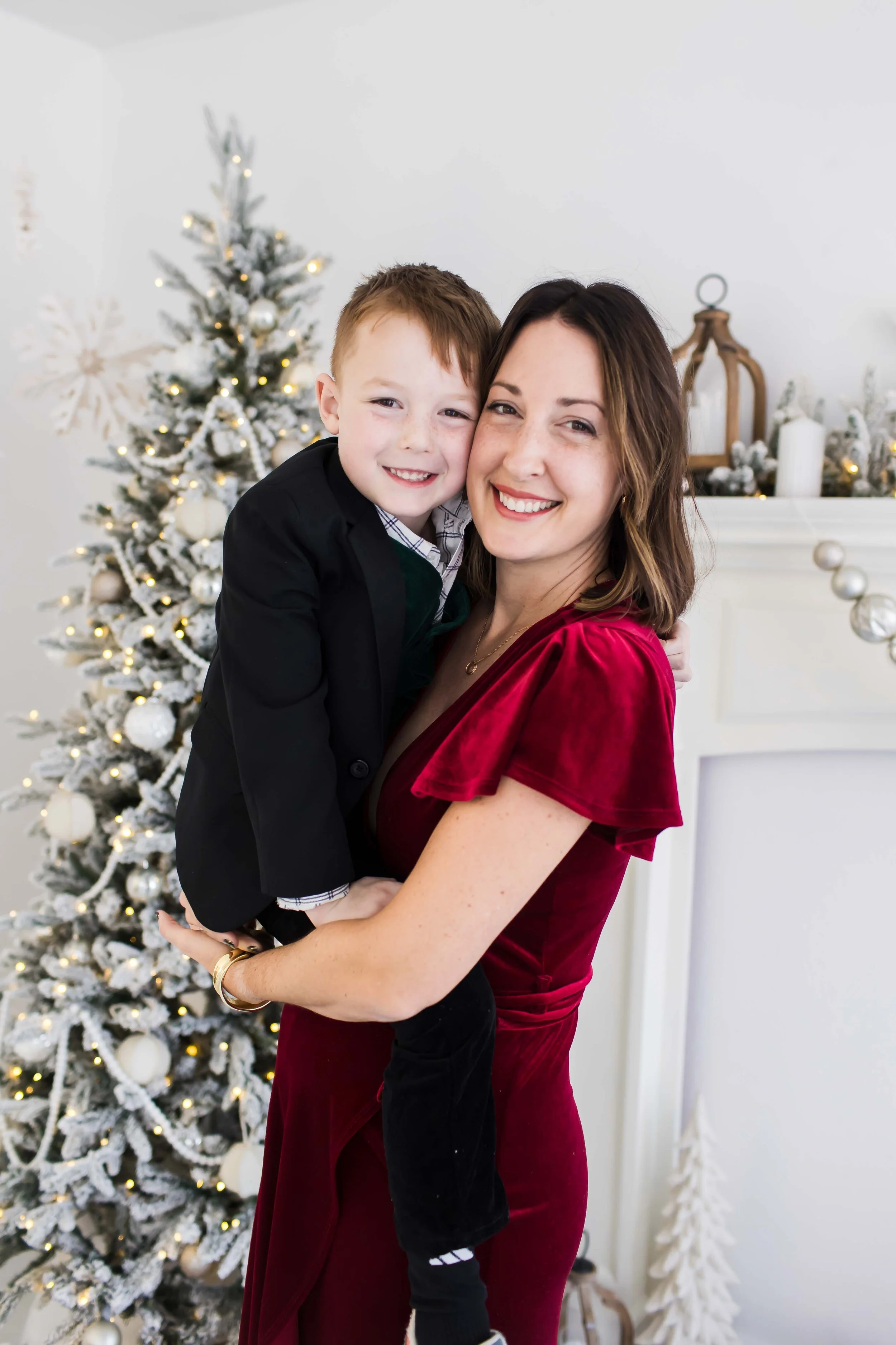 A mom and a young boy smiling and hugging in front of a decorated Christmas tree  at East and Elm Portrait Studio in Fairport, NY, during a Christmas mini session.