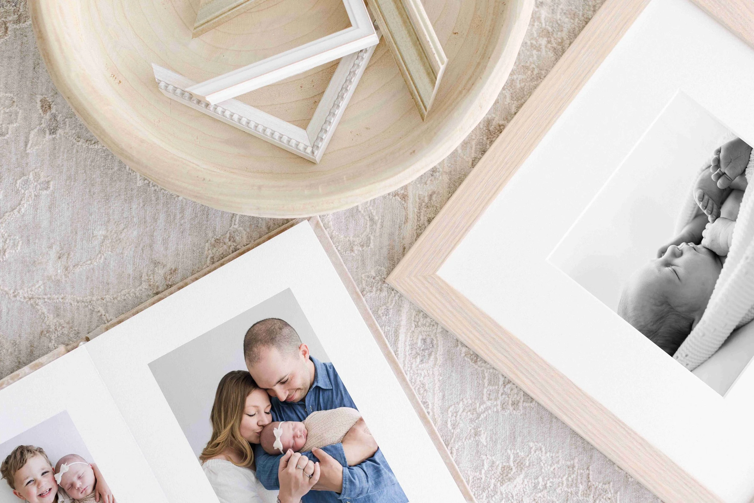 Flat lay of picture frames and photographs on a beige carpeted floor, including a black and white photo of a sleeping baby and a family portrait.
