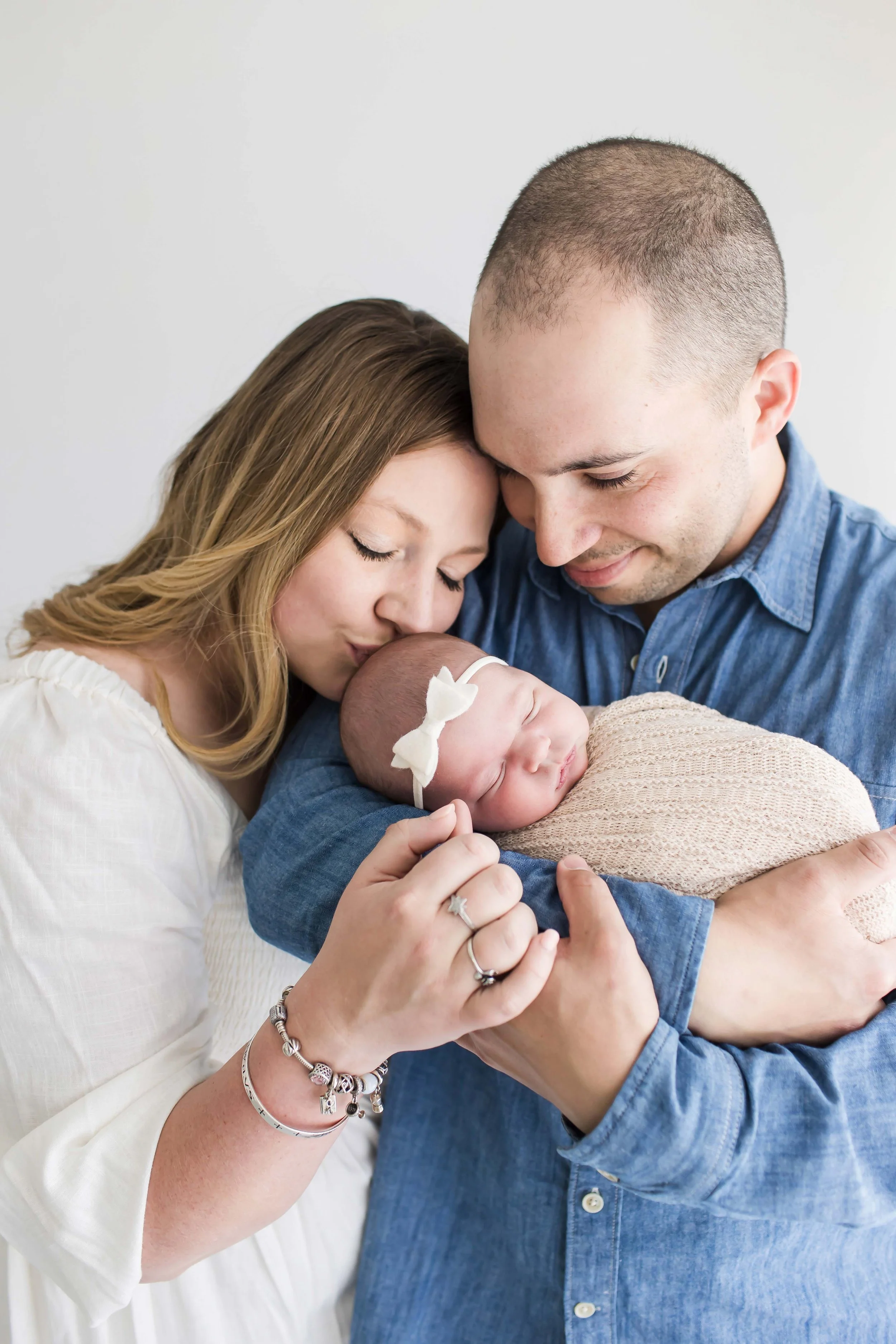 A woman and a man hold a newborn baby close, both with foreheads touching and eyes closed, smiling softly, in an intimate family moment at East and Elm Portrait studio in Fairport, NY.