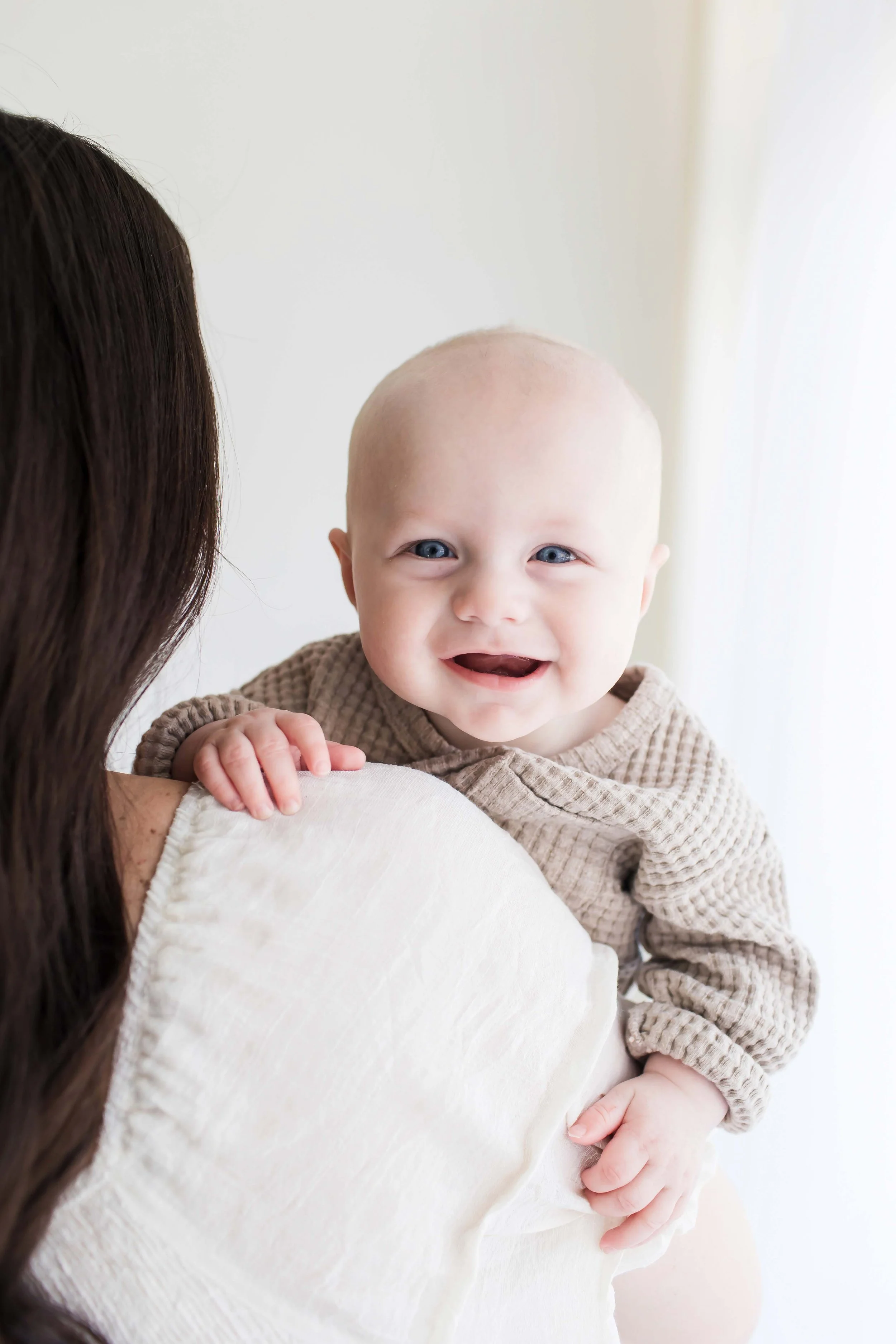 A smiling baby with blue eyes at East and Elm Portrait studio in Fairport, NY, during a family session.