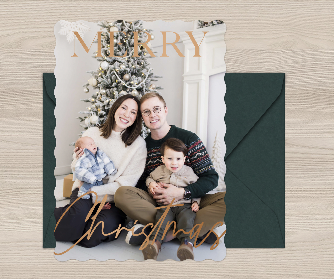 Christmas card with a family of four sitting in front of a decorated Christmas tree, smiling, with overlay text 'Merry Christmas'  at East and Elm Portrait Studio in Fairport, NY, during a Christmas mini session.