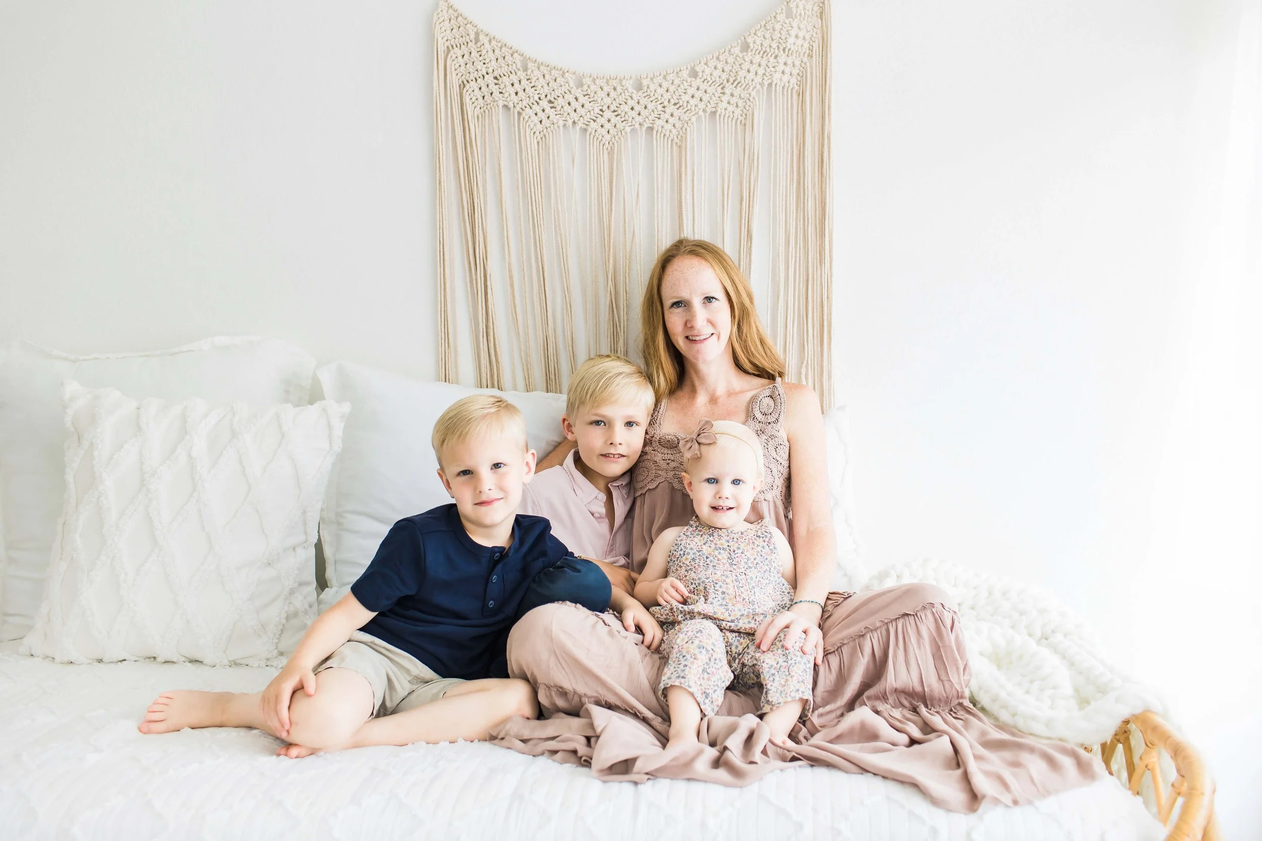A woman with three young children sitting on a bed at East and Elm Portrait Studio in Fairport, NY, during a family session.