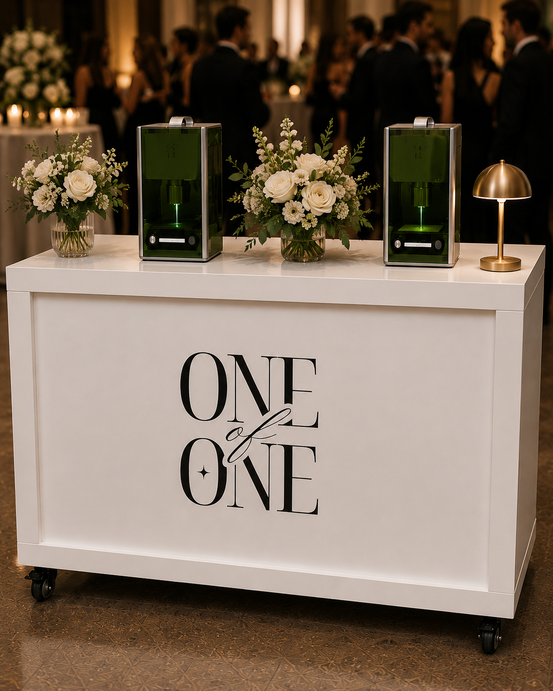 A wedding reception sign reading 'one of a kind' on a white counter with two flower arrangements, two green drink dispensers, and a gold lamp, with guests dancing in the background.