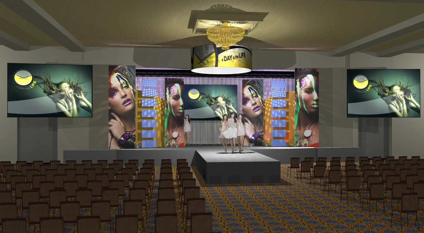 An indoor stage setup with large screens displaying artistic images of women, rows of chairs facing the stage, and three women in white dresses standing on the stage.