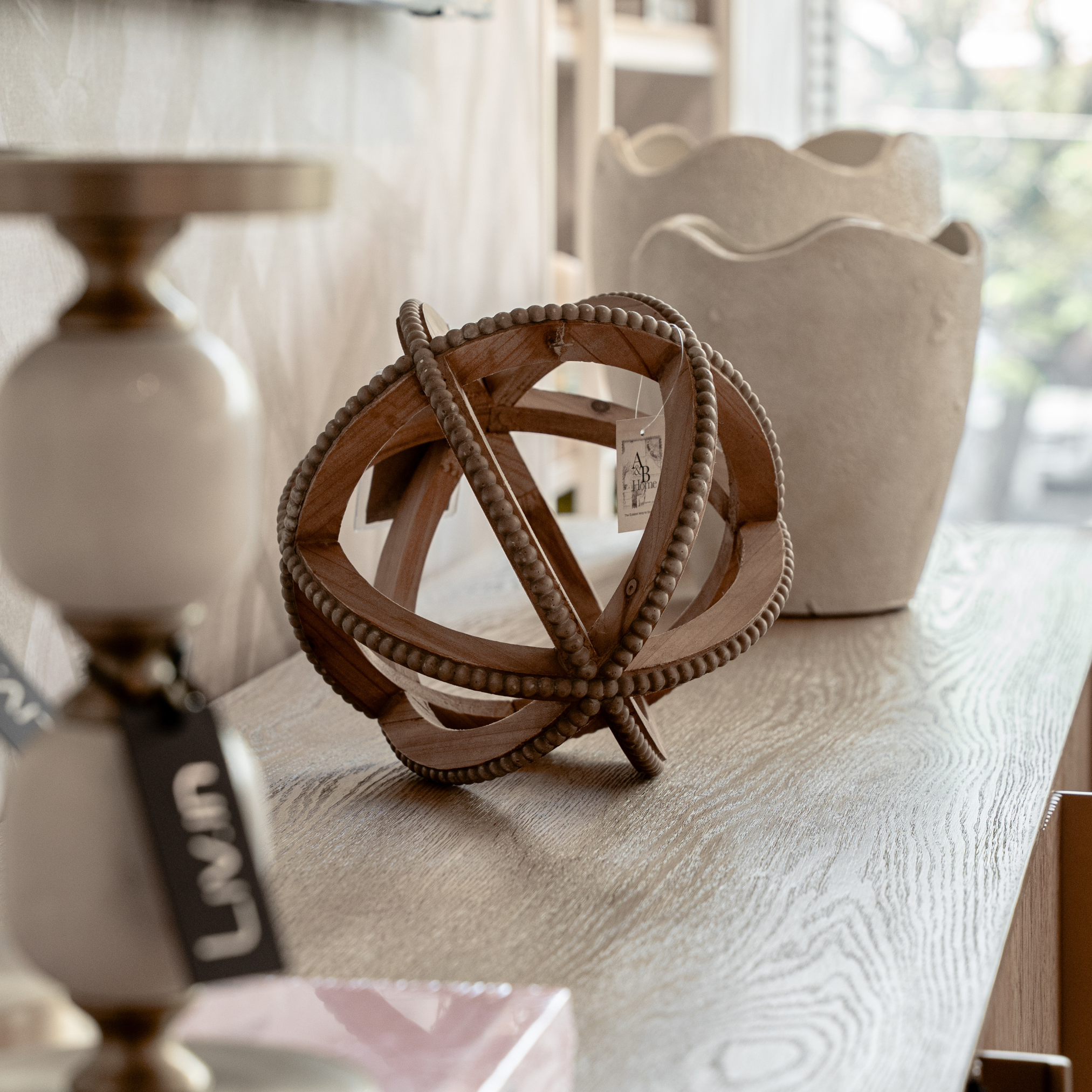 Wooden jewelry display with beaded jewelry and a tag, blurred background with shelves and natural light.