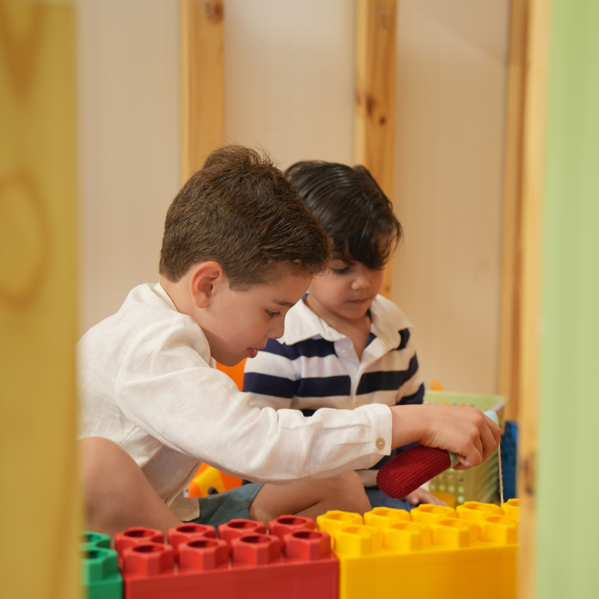 Two boys focused on playing with colorful building blocks in a play area with a wooden background.