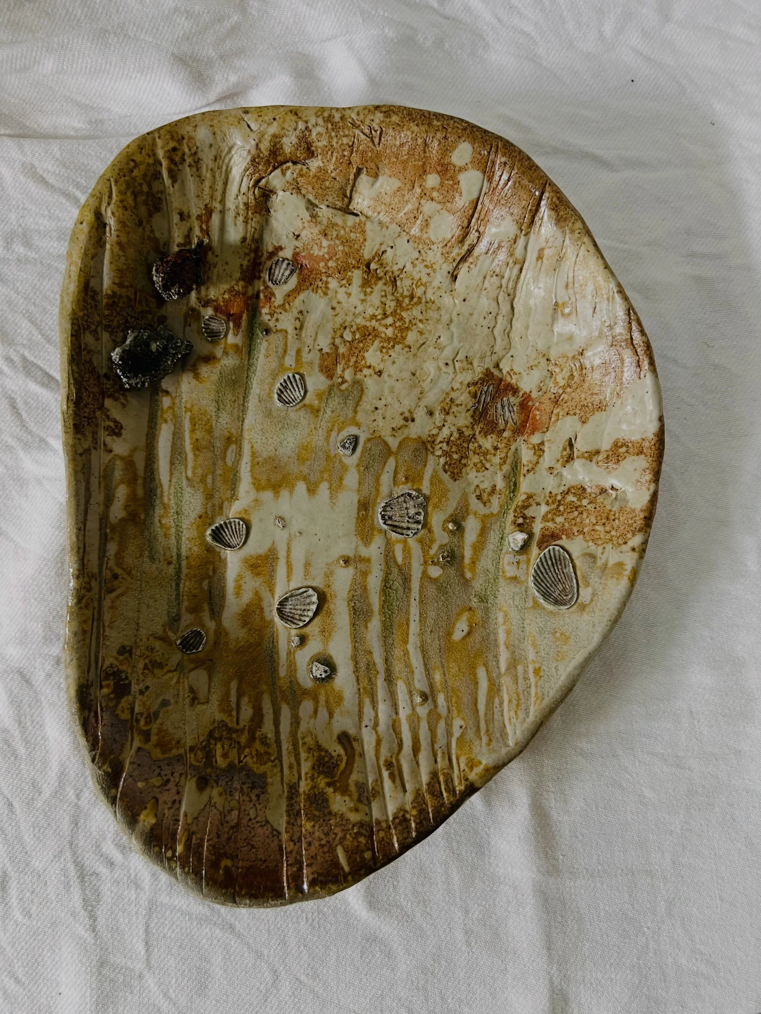 An imprint of the red cedar from @oxfordkilns , and shells unused under other pieces to protect against the ash sticking everything together. This makes for a complex surface on this dish. Not to mention the extra bits of matter that have floated aro