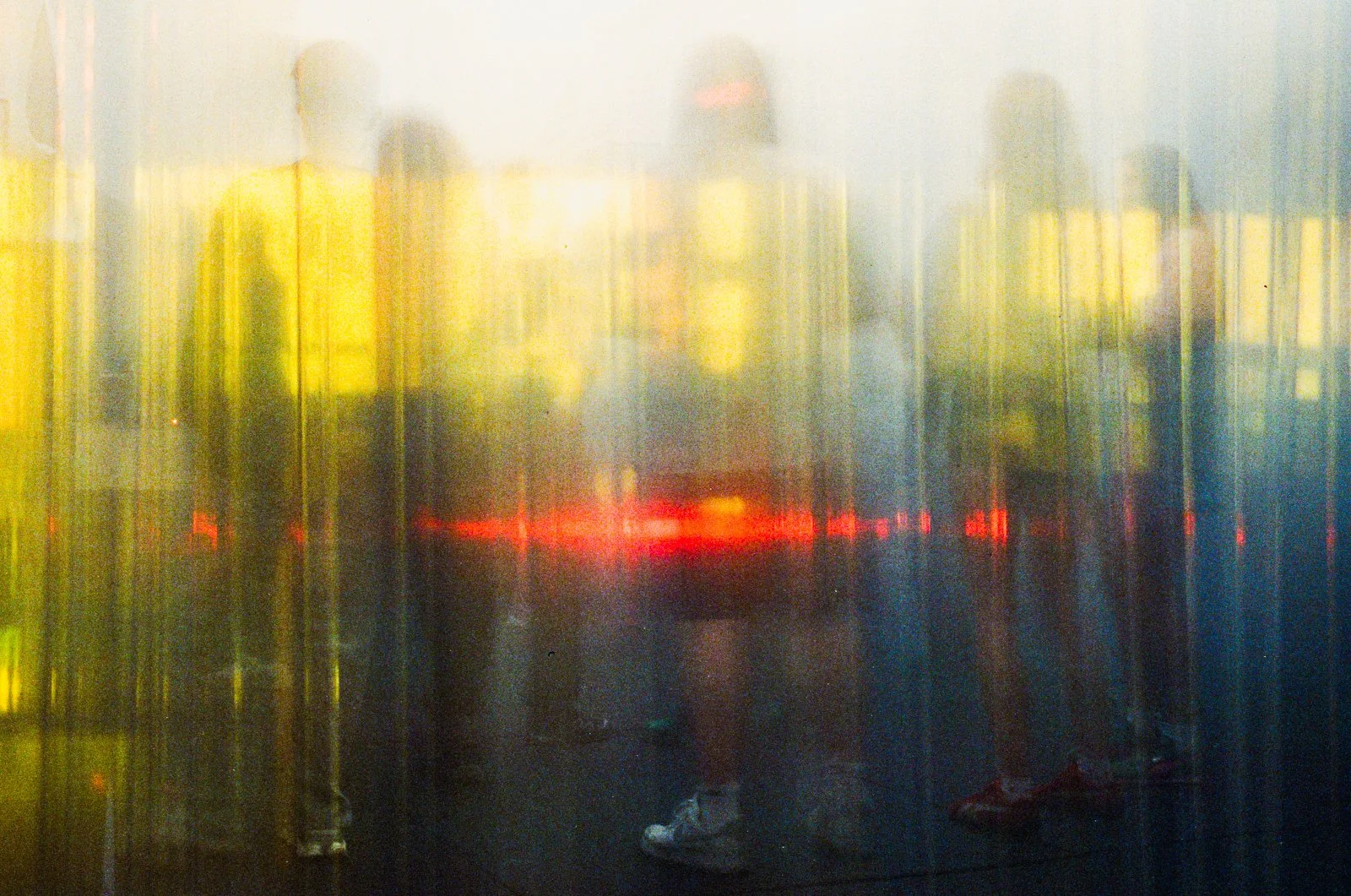 Reflections of people and city lights on a wet glass surface at dusk or night.