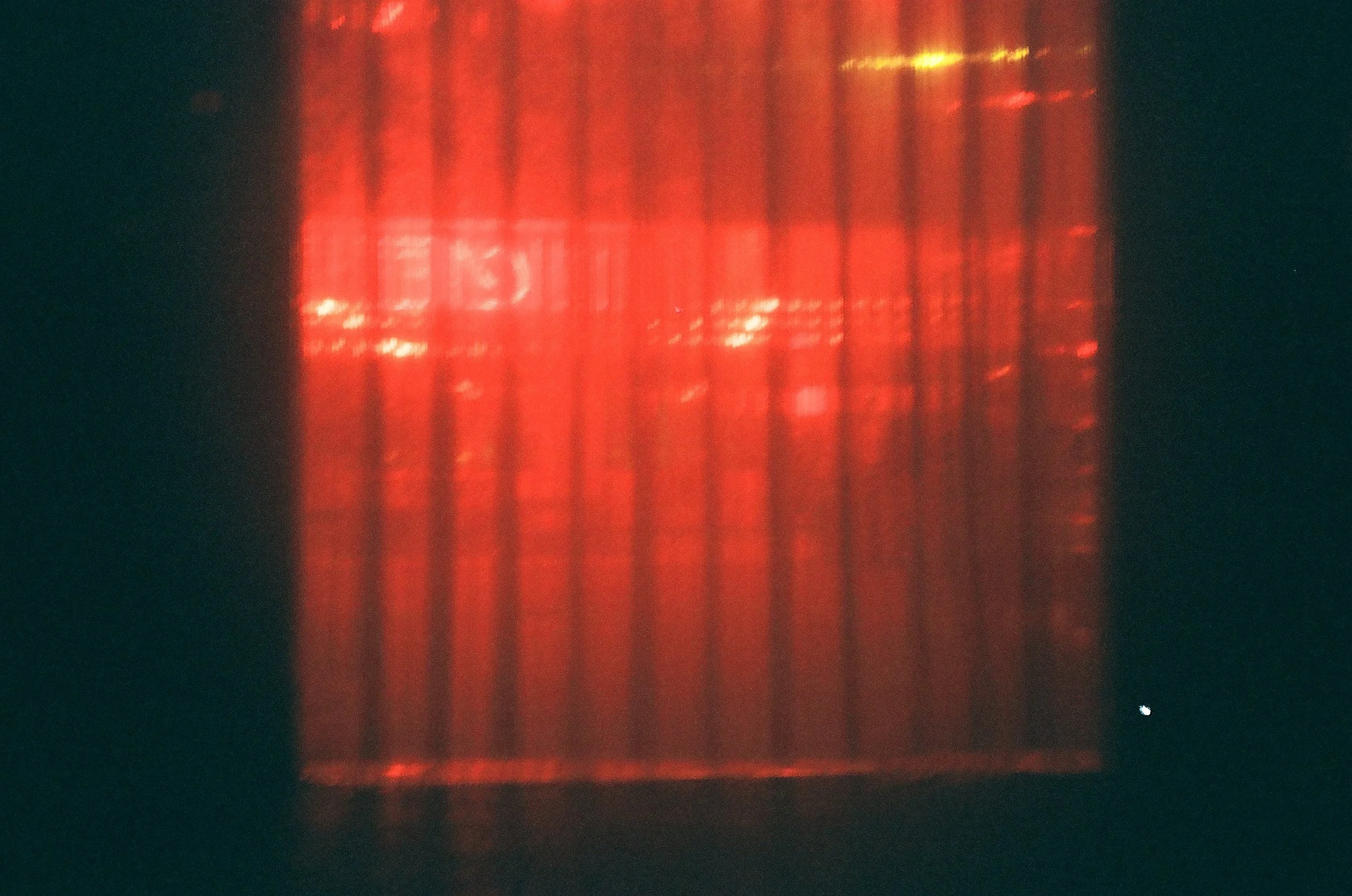 A red rectangular object with evenly spaced vertical lines or bars, illuminated from behind, creating a glowing effect. The background is dark.