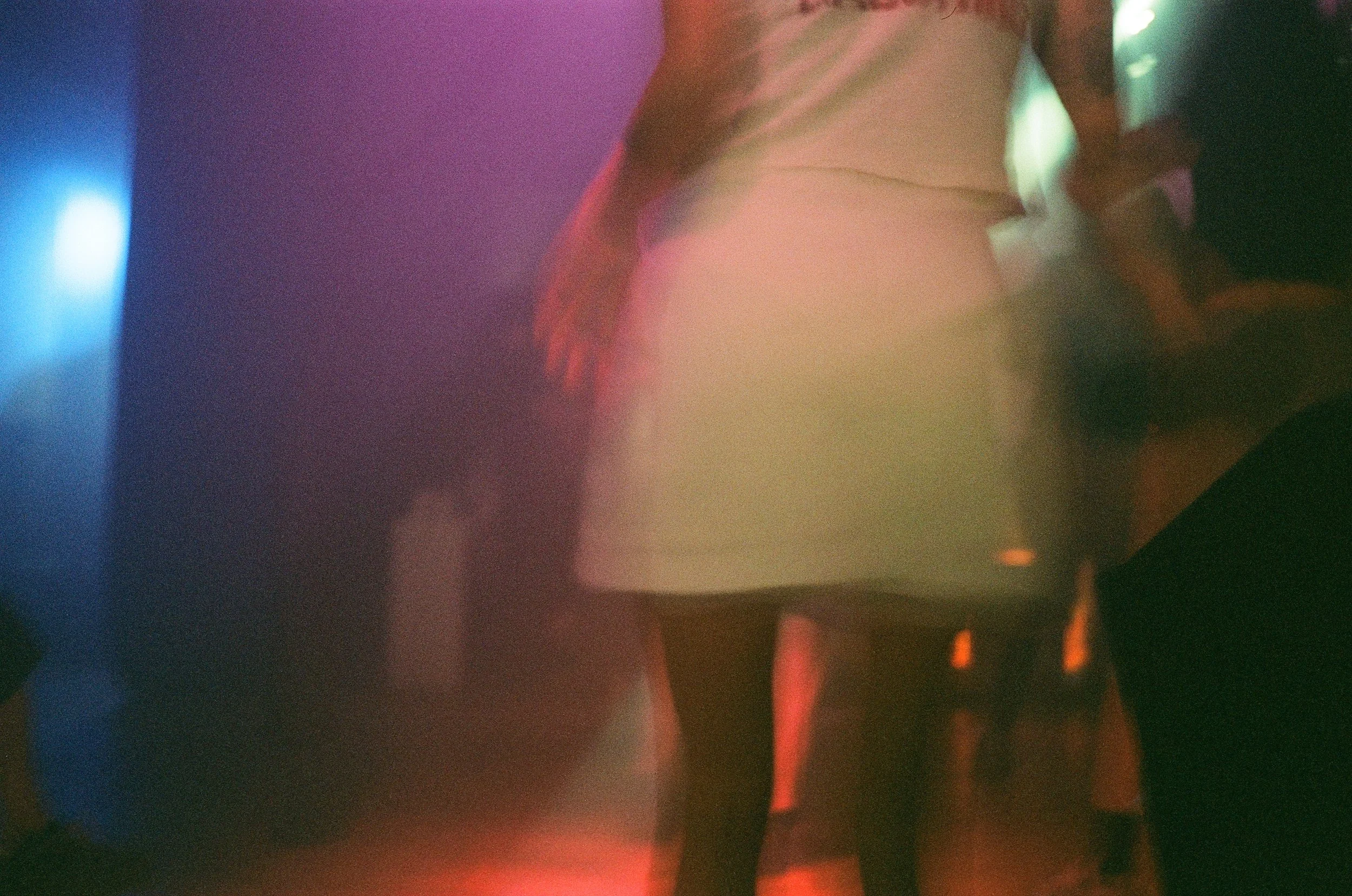 Blurred abstract scene with colorful lights and shapes, possibly depicting a nightclub or concert environment with purple, blue, green, and orange hues.