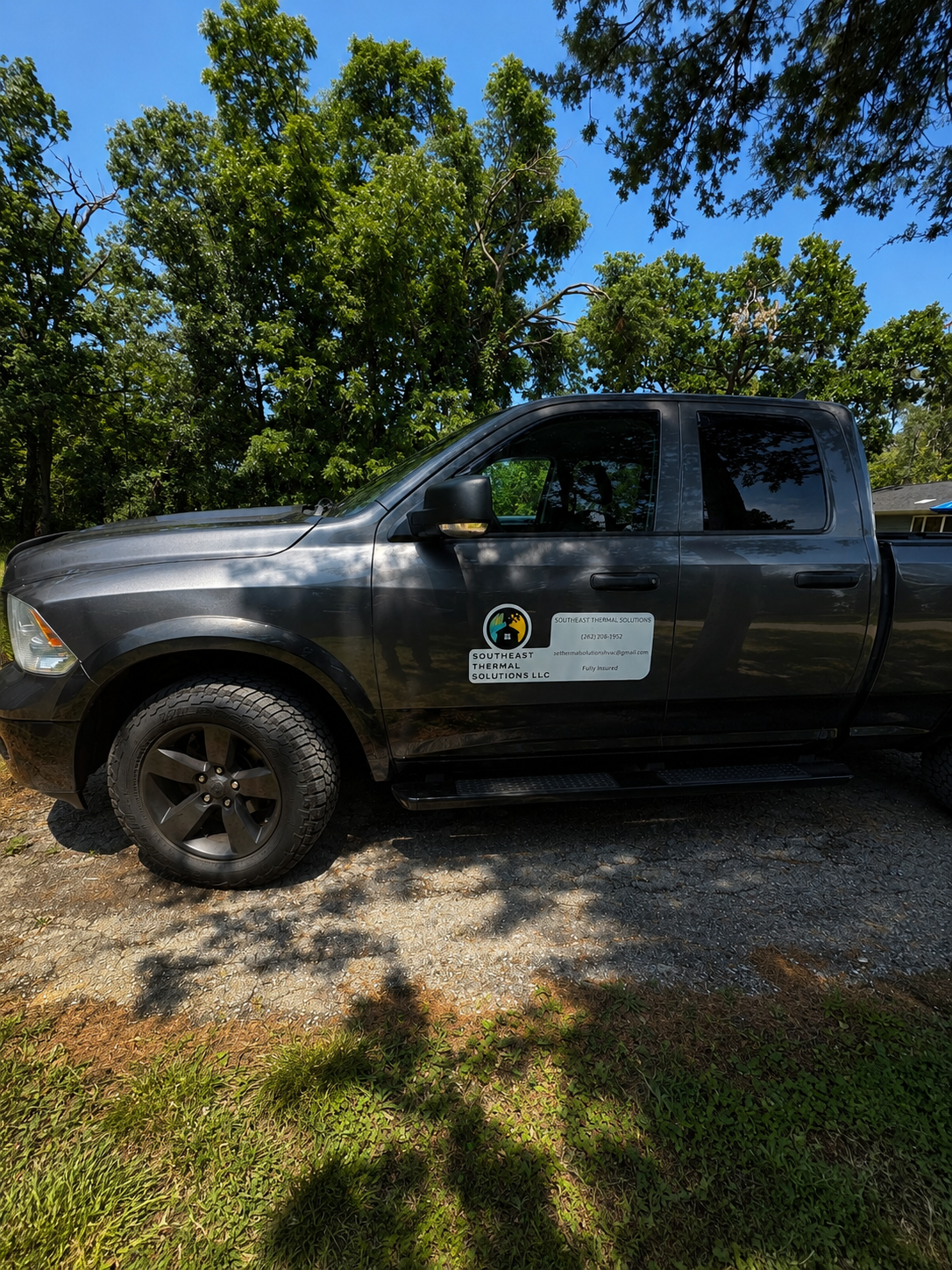A black pickup truck with a company logo for Southeast Thermal Solutions parked outdoors under trees on a sunny day.