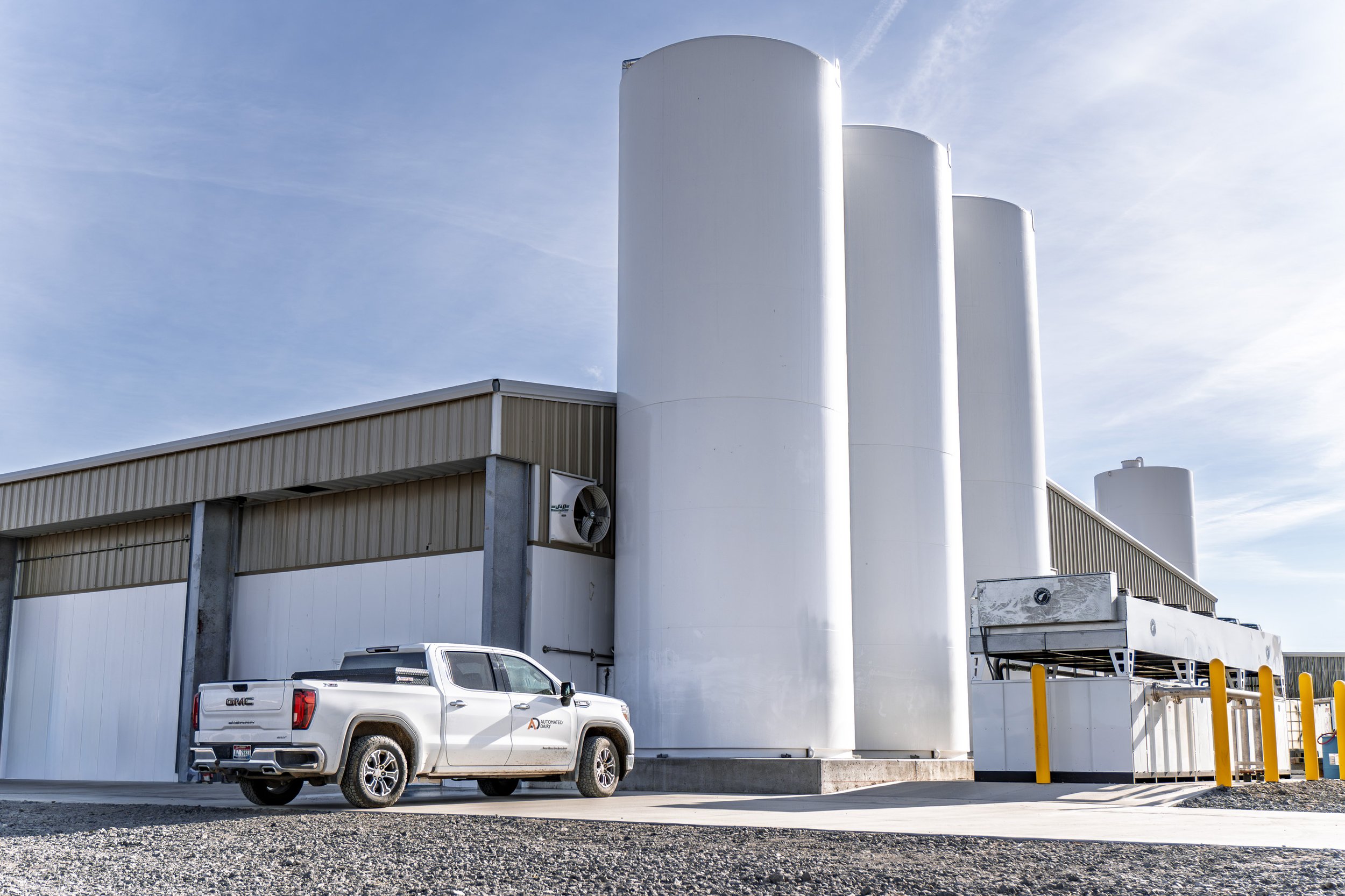 A white Automated Dairy GMC pickup truck parked in front of a large dairy.