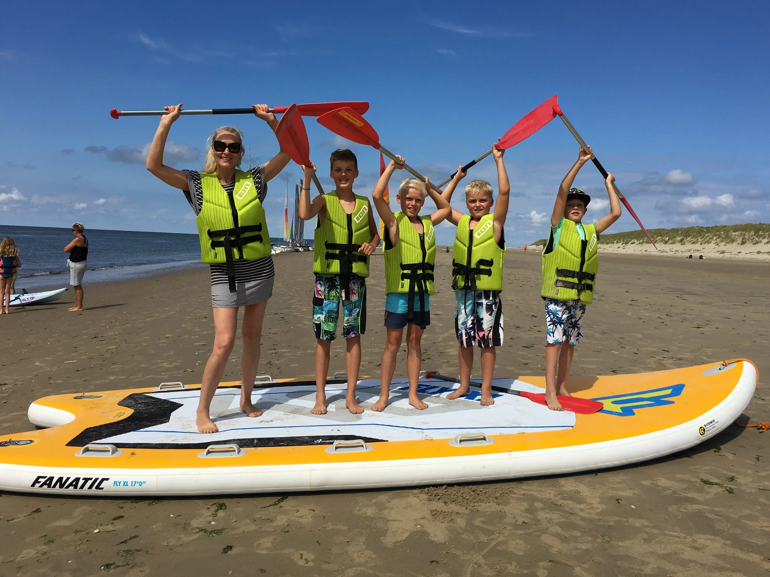 Kinderen in reddingsvesten op een suppboard op het strand van Ameland