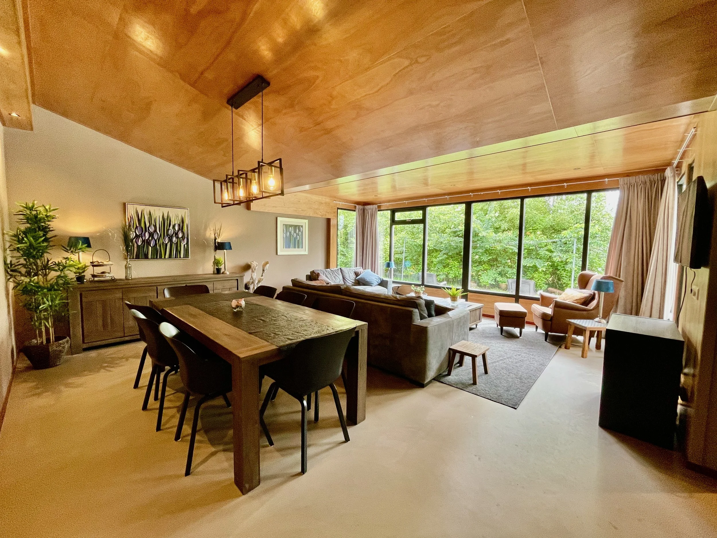 Woonkamer met houten eettafel, zithoek en houten plafond in Bungalow Sonnevanck in Ballum op Ameland