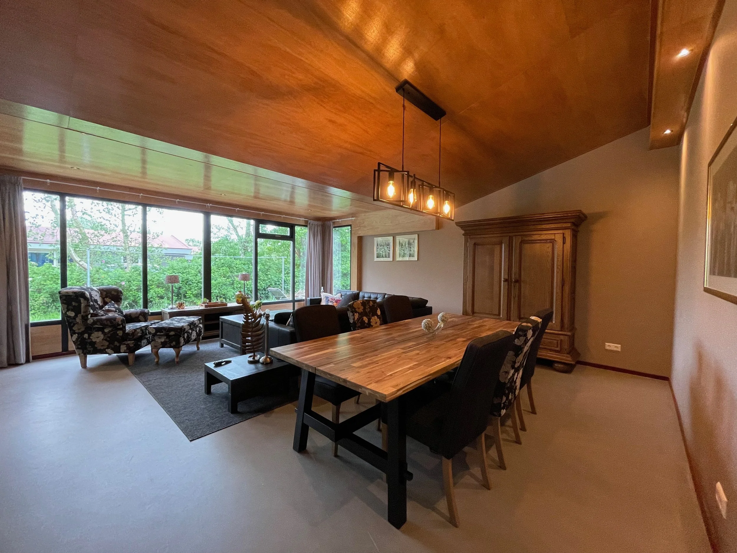 Woonkamer met houten eettafel, zithoek en uitzicht op het groen in Bungalow Luitekamp in Ballum op Ameland
