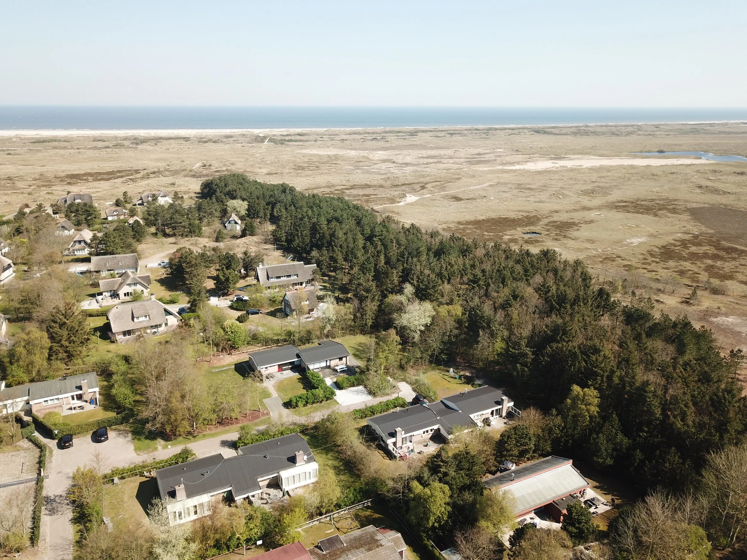 Luchtfoto van de vier vakantiehuizen tussen bos en duinen in Ballum op Ameland met het wad op de achtergrond