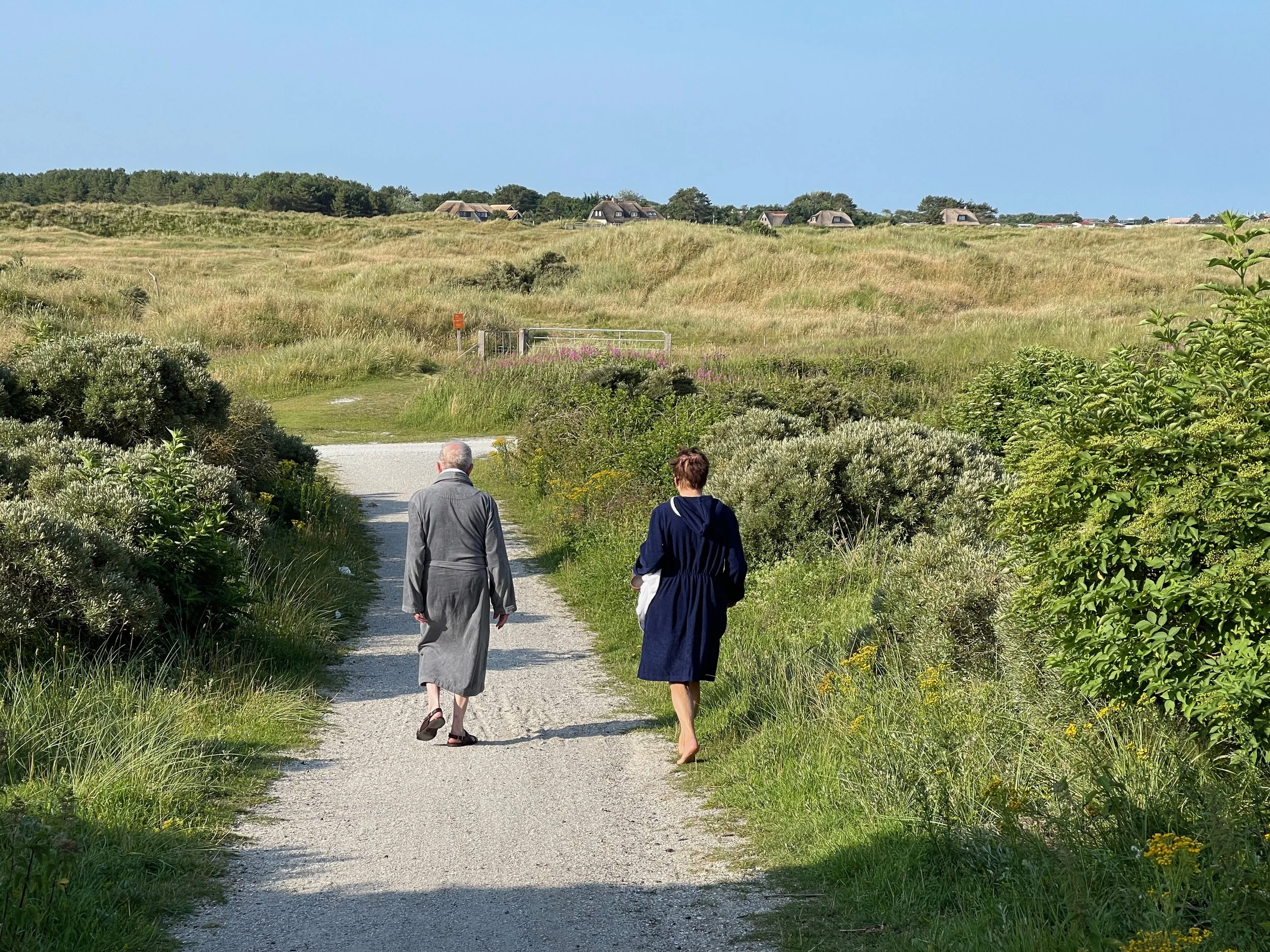 Twee mensen in badjas lopen over een schelpenpad door de duinen van Ameland