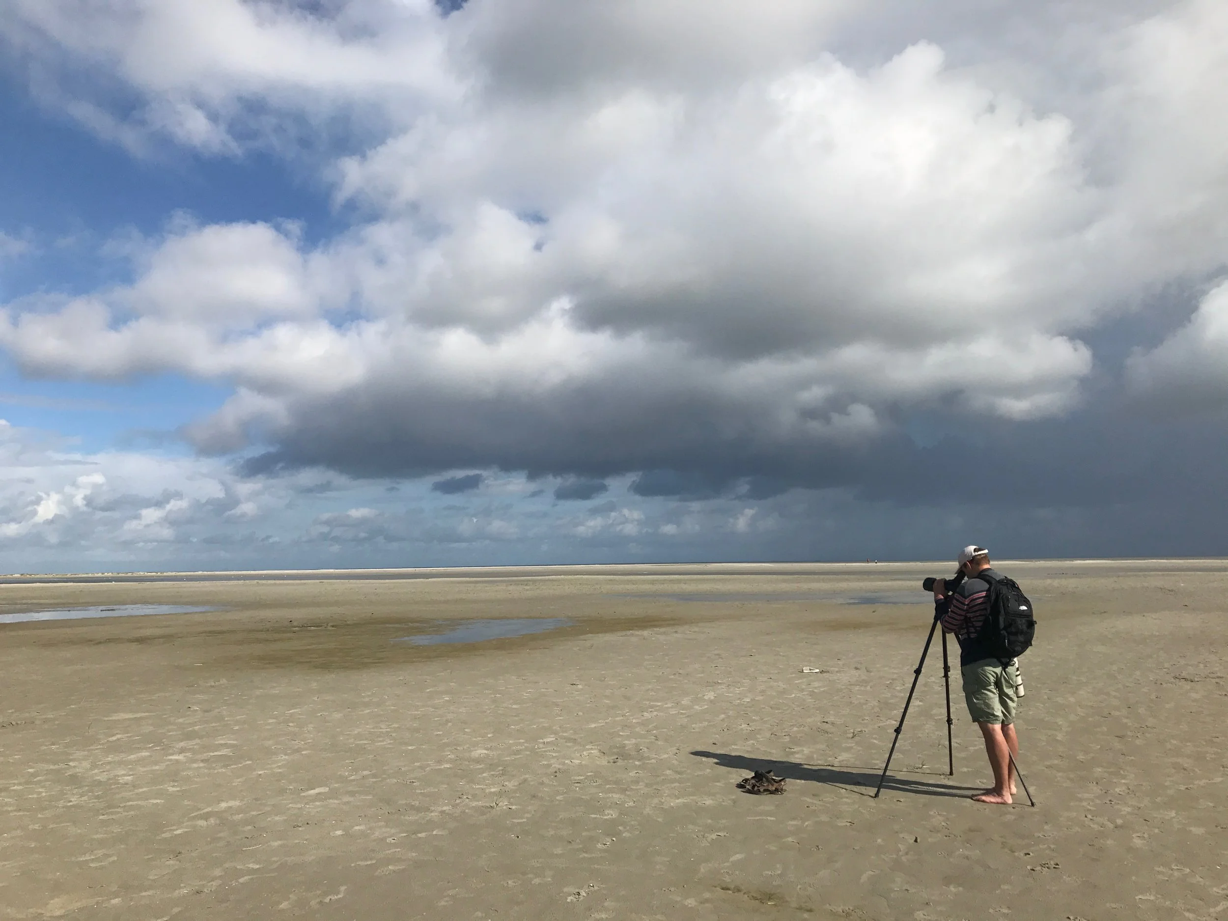 Wolkenlucht boven het wad bij Ameland met een wandelaar op het droogvallende strand