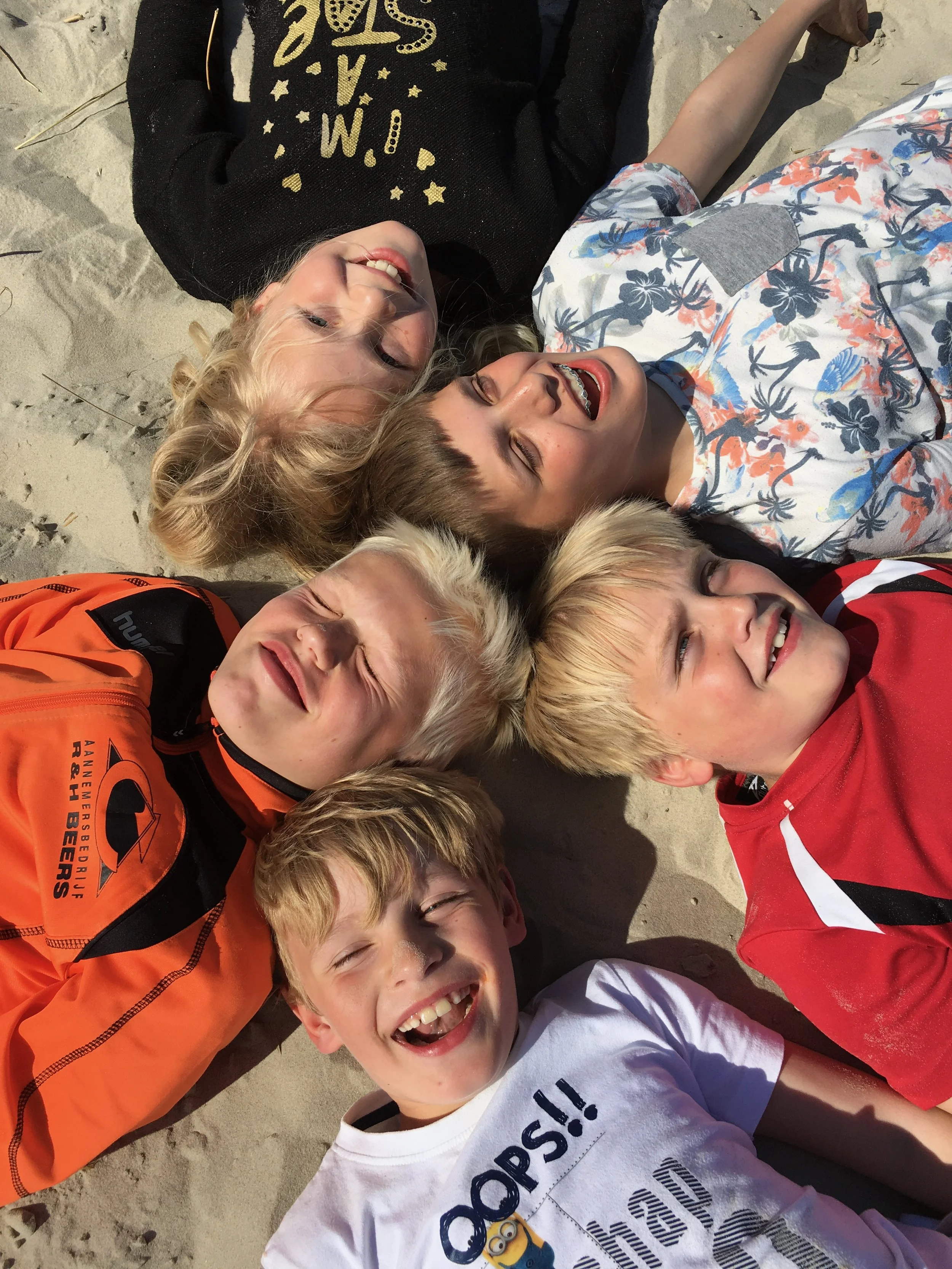 Familie ligt lachend in een kring in het zand op het strand van Ameland