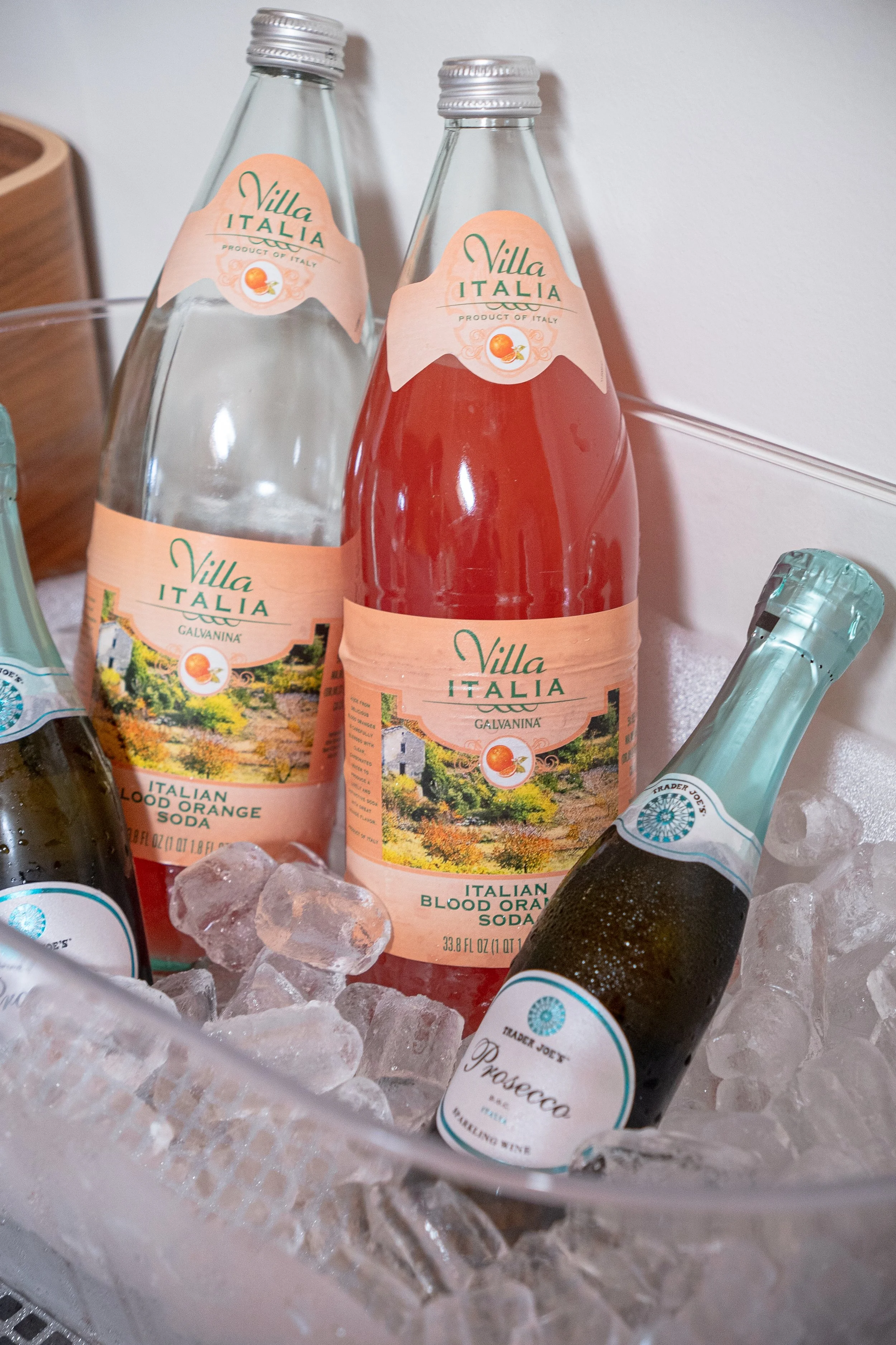 Bottles of Villa Italia blood orange soda and Trader Joe's prosecco on ice, in a clear container with ice cubes.