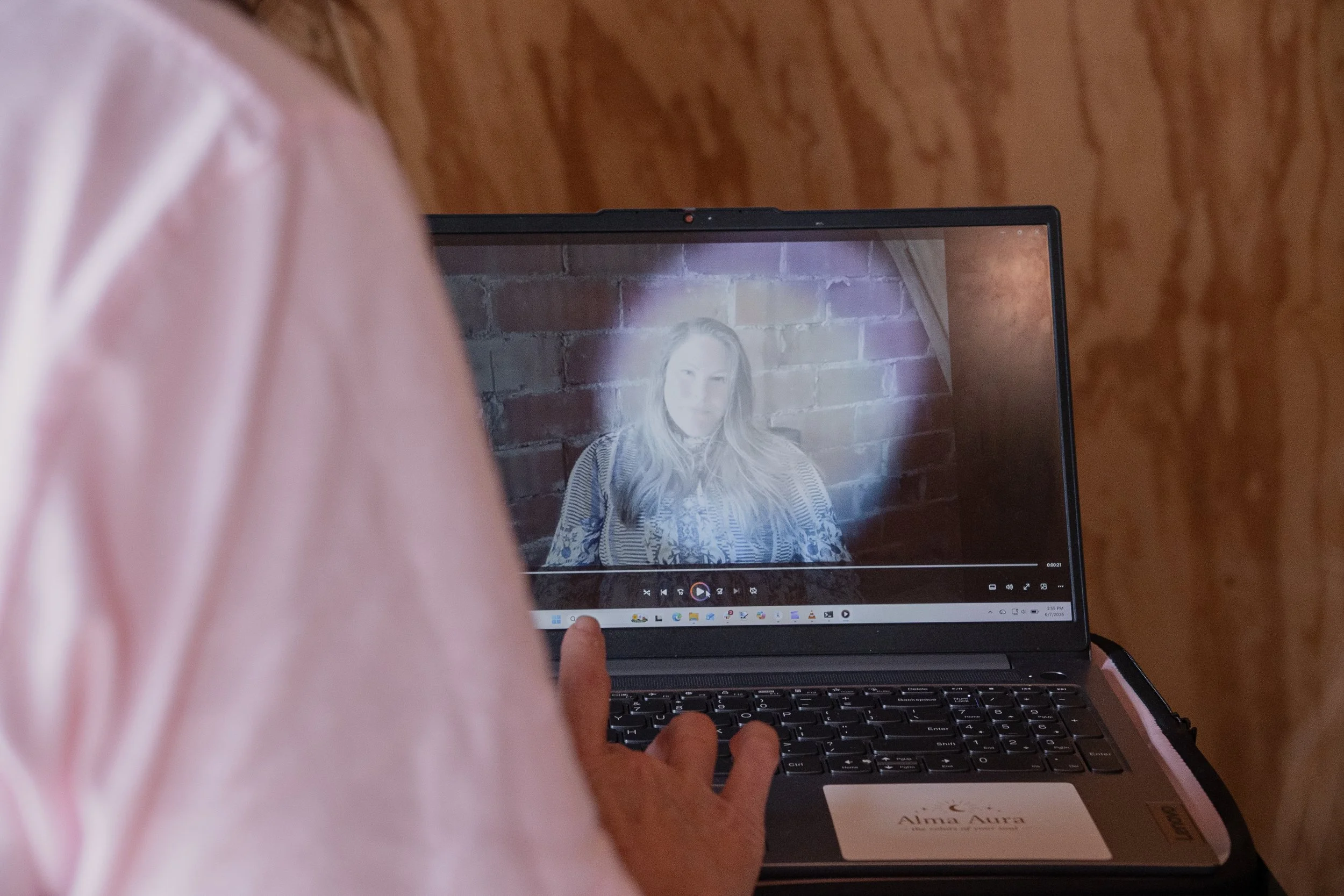 A person interacts with a laptop displaying a woman with long hair against a brick wall background.