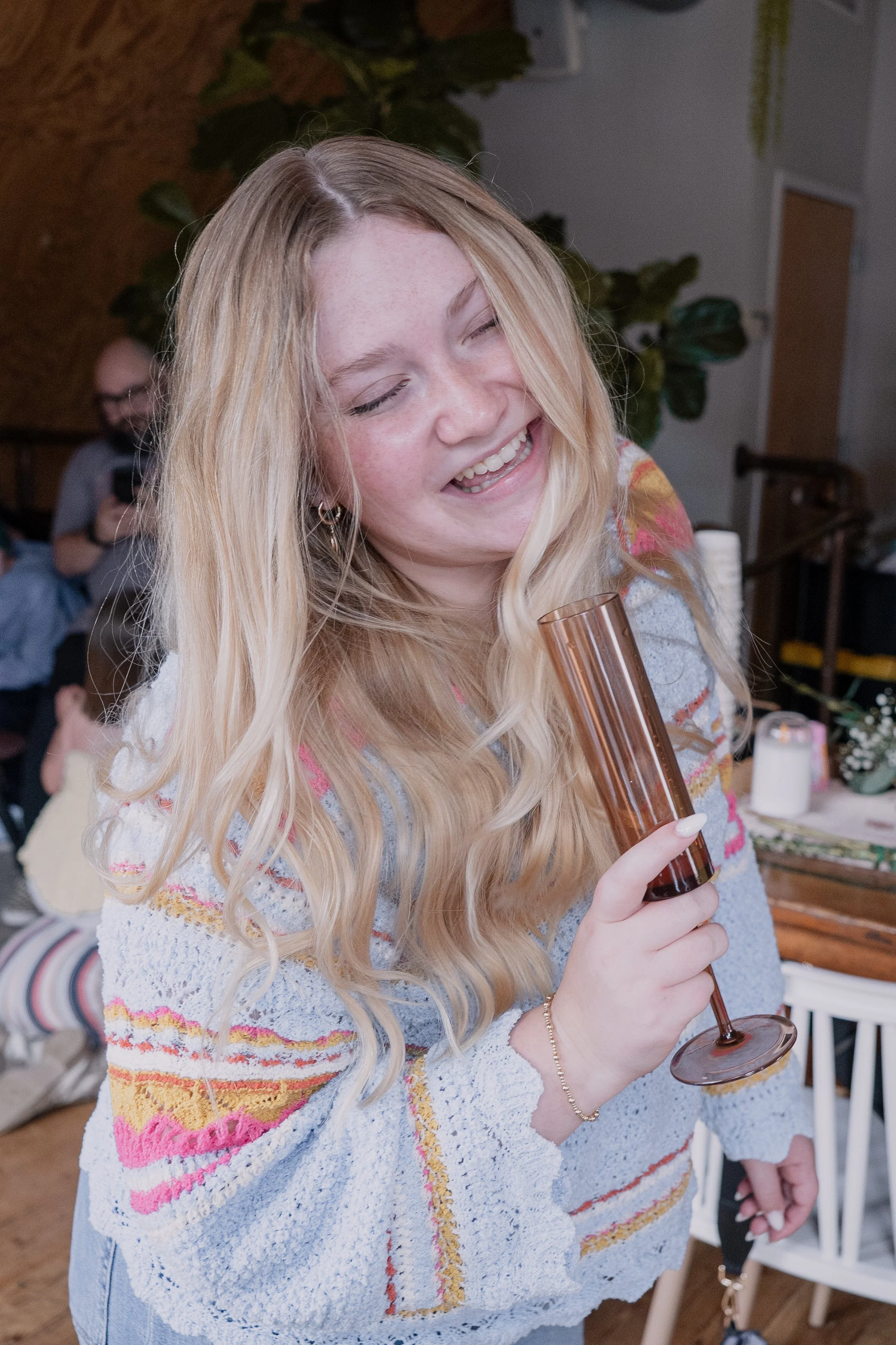A woman with long blonde hair smiling and holding a glass of champagne at a social gathering.
