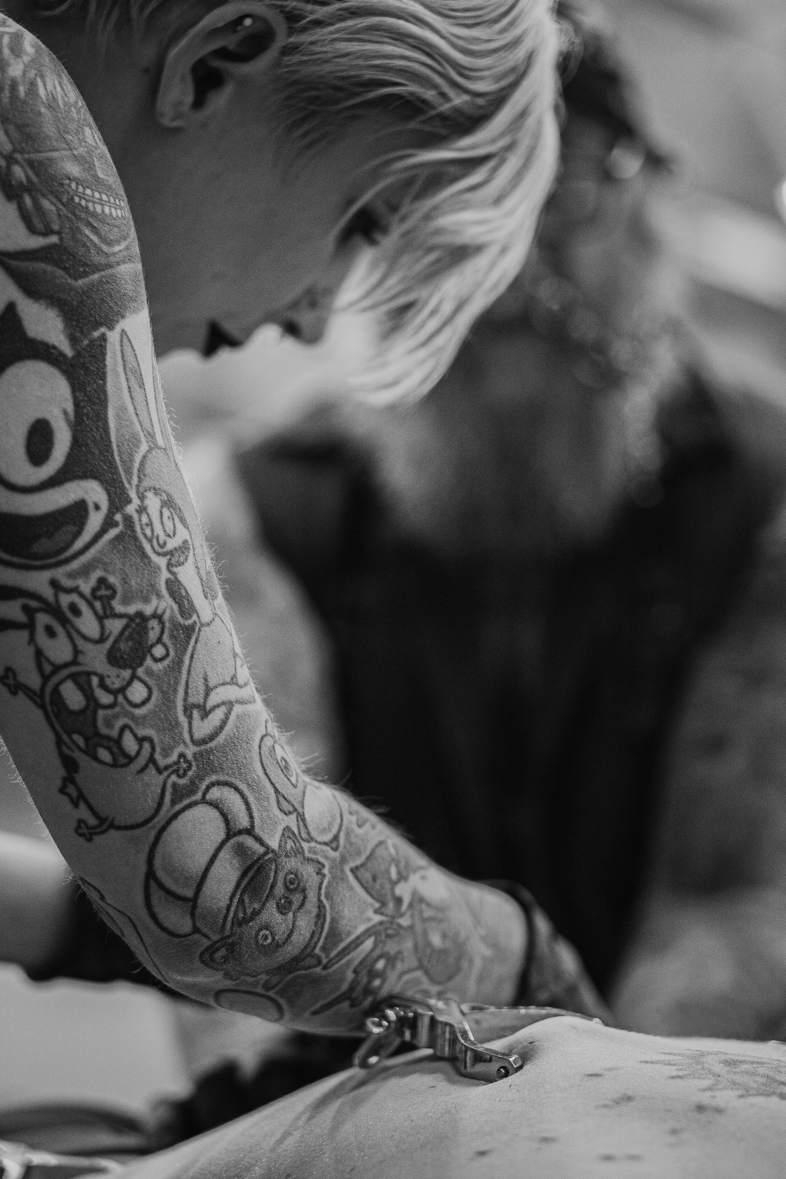 Close-up photo of a person's arm with a detailed tattoo, using a medical device on their skin, in black and white.