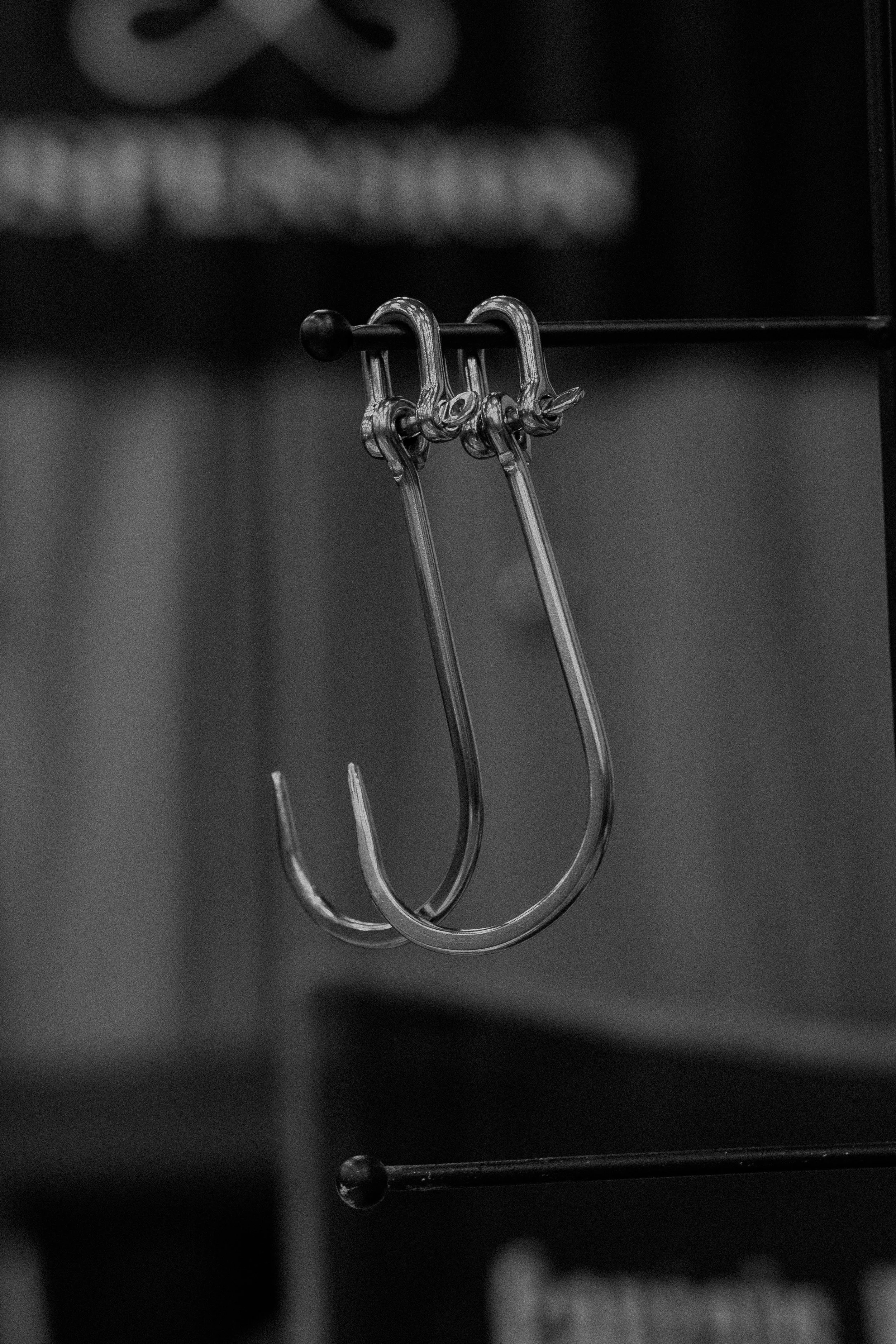 Close-up of a pair of metal hooks hanging from a black horizontal rod, with blurred background.