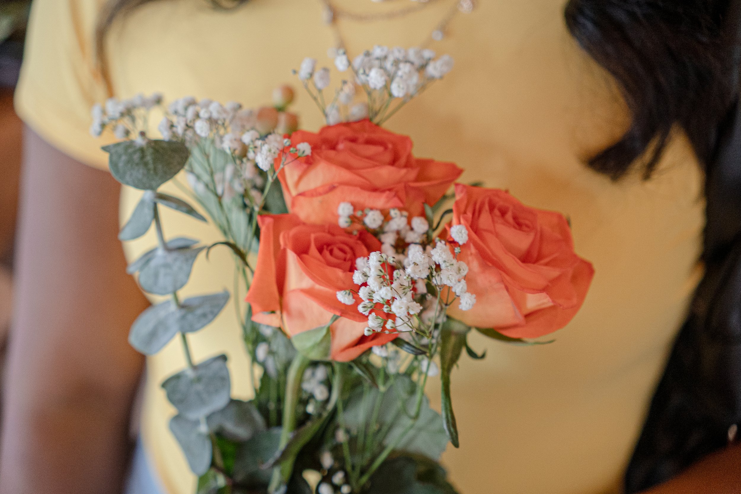 A bouquet of orange roses with white baby's breath and green foliage on a yellow surface.
