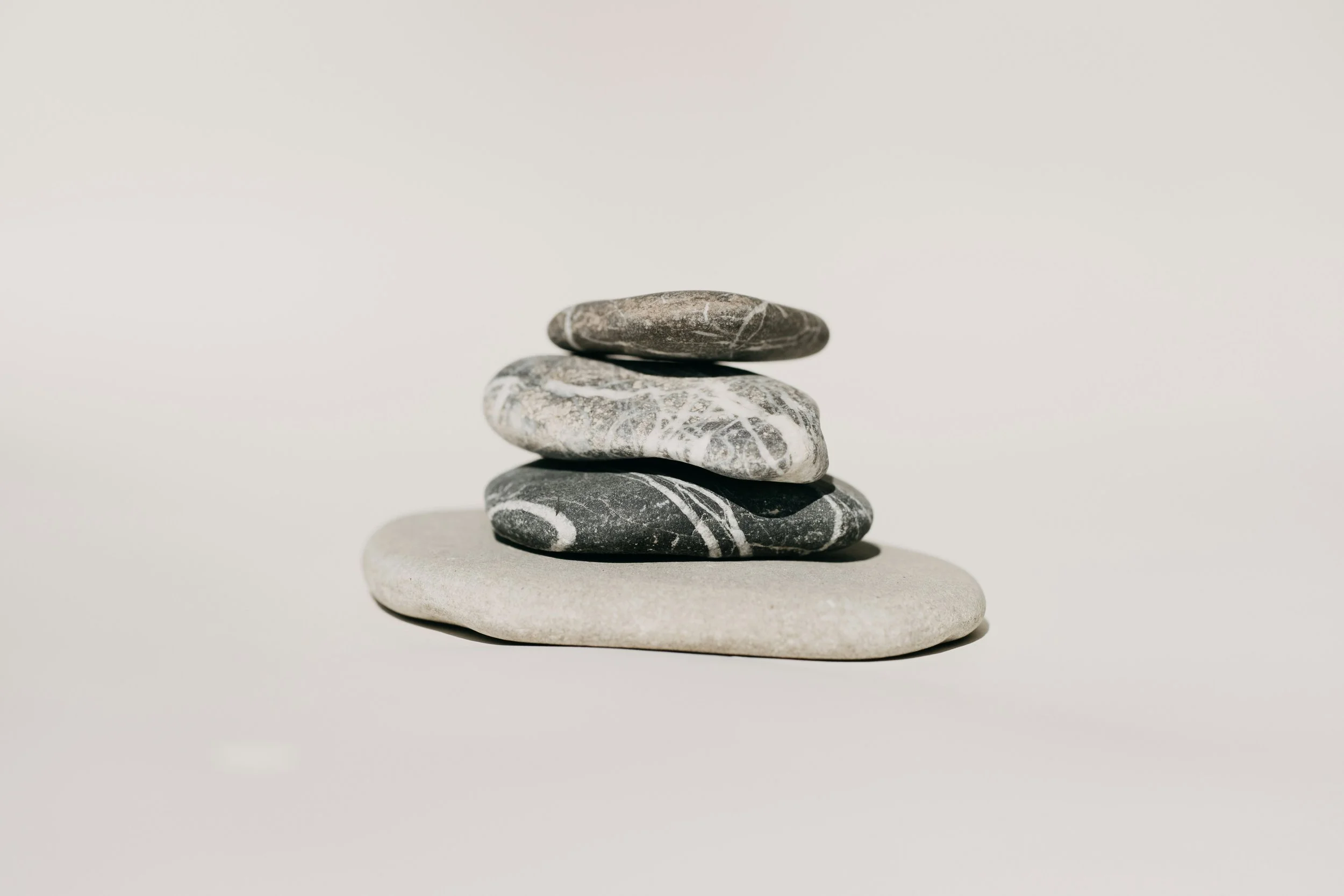 A stack of five stones, with the bottom stone being smooth and white, and each stone above it dark gray with white veining, against a plain light background.