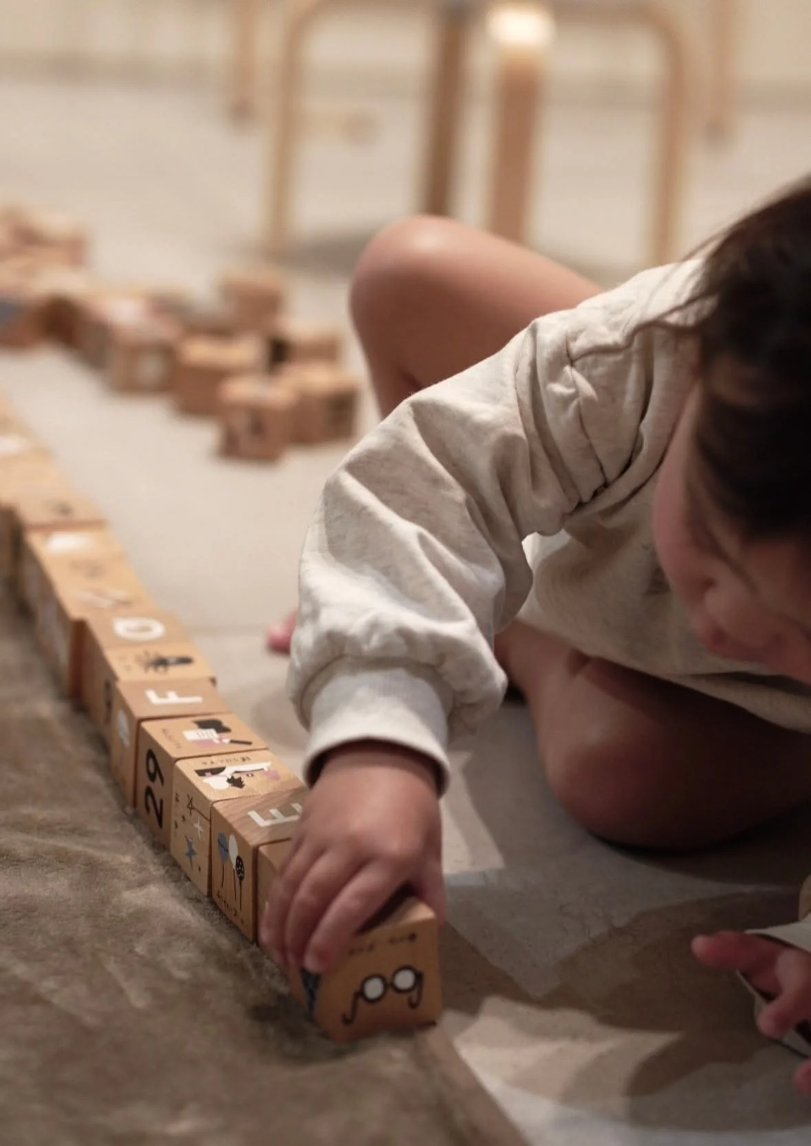 A child kneeling on the floor, playing with wooden blocks with animals, numbers, and letters on them, arranged in a line.