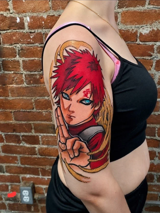 Tattoo of a character with red spiky hair, intense blue eyes, and a red mark on the face, holding a hand in a gesture, on a woman's upper arm, against a brick wall background.