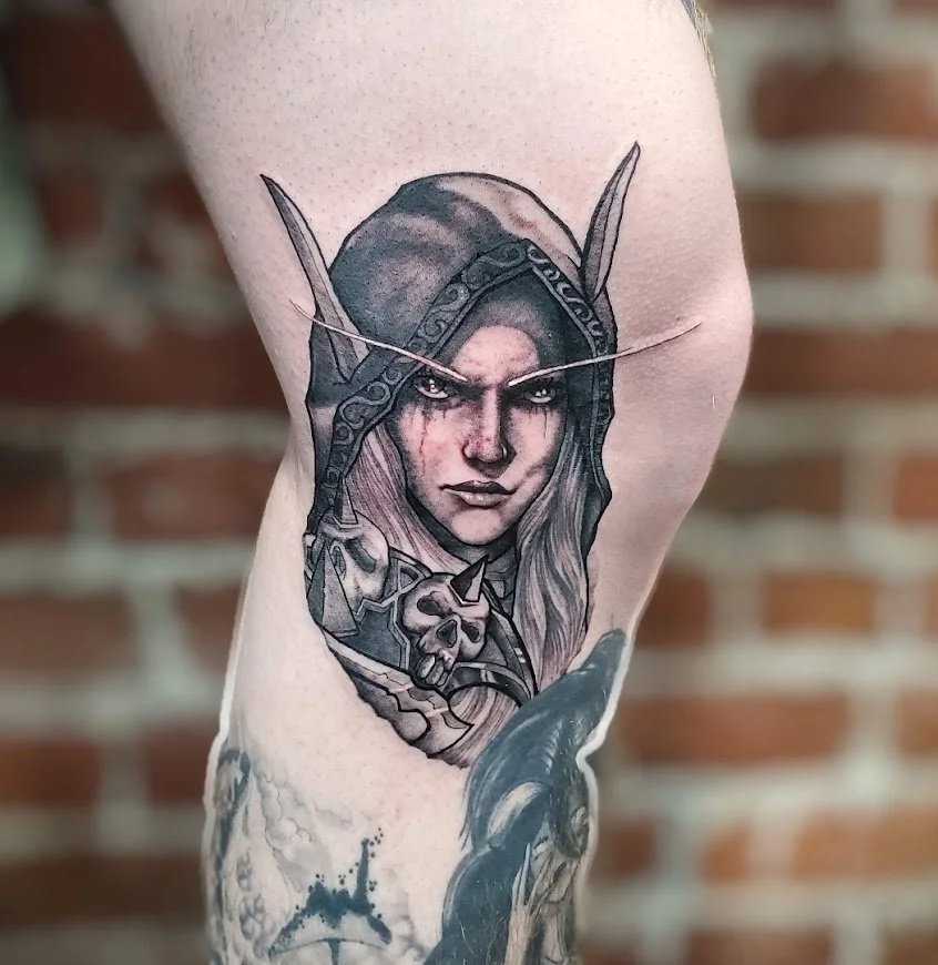 Tattoo of an elf woman with long hair and pointed ears, wearing a hooded cloak, with a stern expression, surrounded by skulls and fantasy elements.