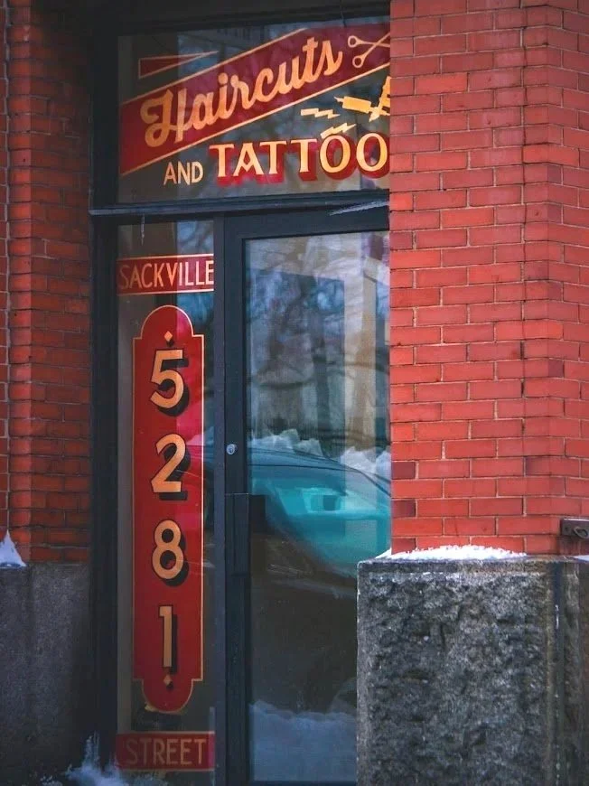 Sign outside a brick building advertising a haircuts and tattoo shop with a phone number 528-81, and street name Sackville Street.