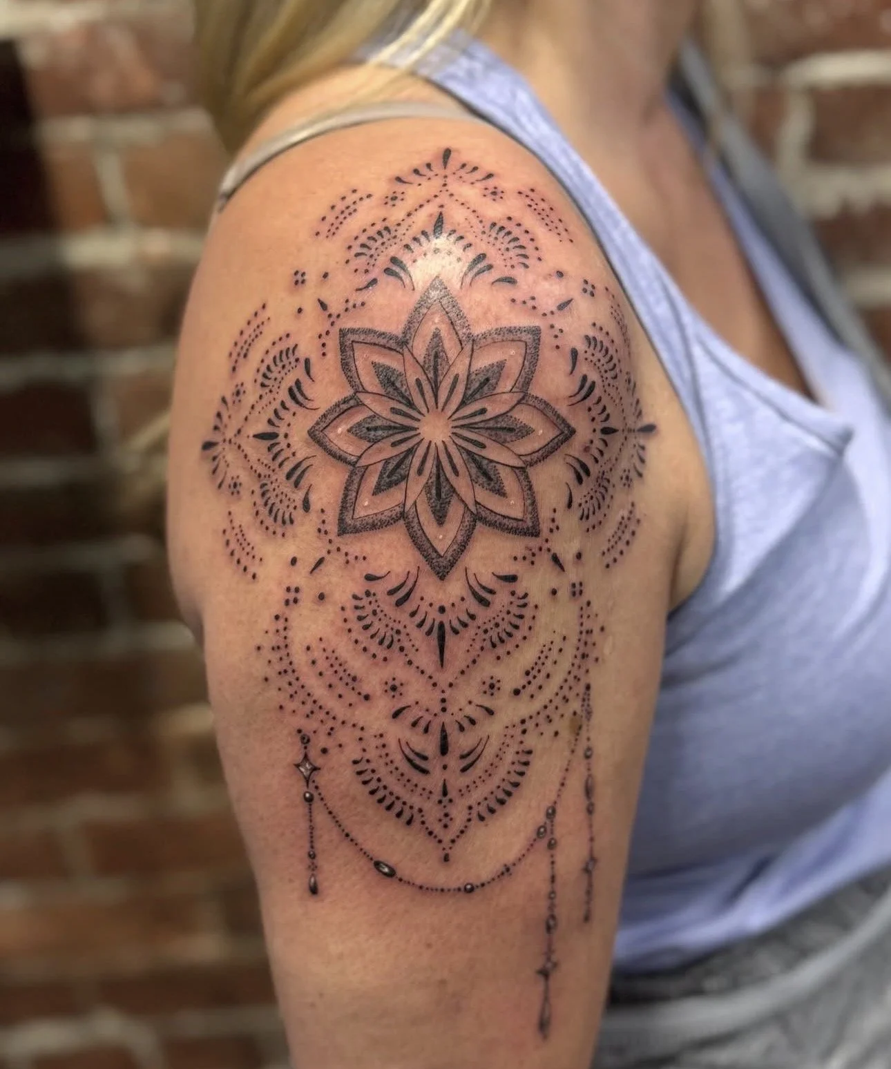 Black and gray geometric mandala tattoo on upper arm, with intricate linework and dotwork details.
