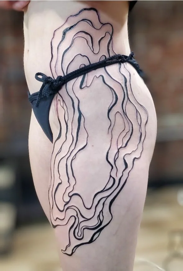 A person's side with a tattoo of cyber sigilism topographic map lines extending from their waist to their thigh, partially covered by a black bikini bottom.