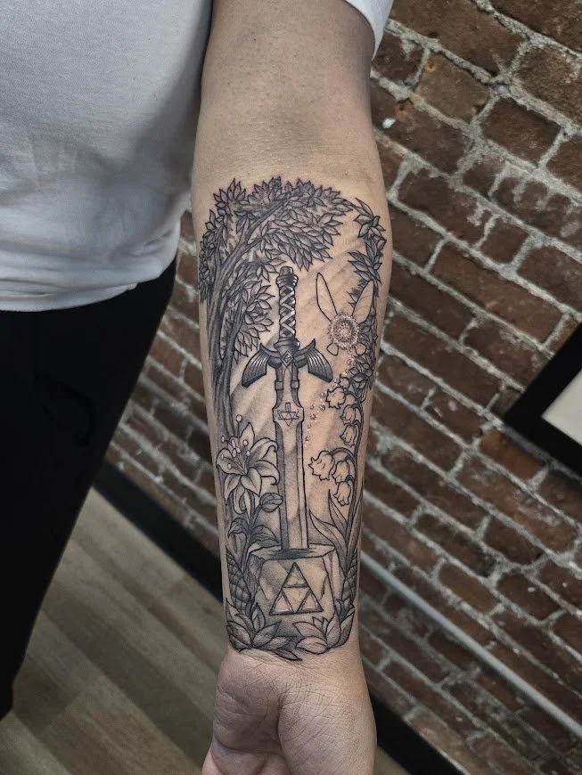 Black and gray tattoo of a sword in a tree, with floral and nature elements surrounding it, on a person's forearm. the legend of Zelda