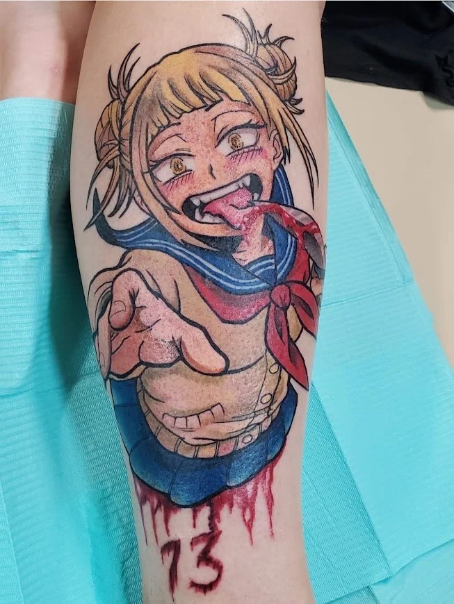 Colorful tattoo of a girl with blonde hair in sailor school uniform, making a silly face with her tongue out and eyes wide open, on a person's arm.