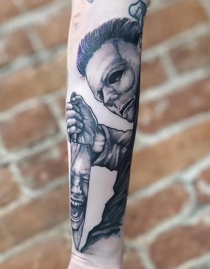 Black and gray tattoo on forearm depicting a person with a mohawk hairstyle, wearing a mask and holding a crying face.
